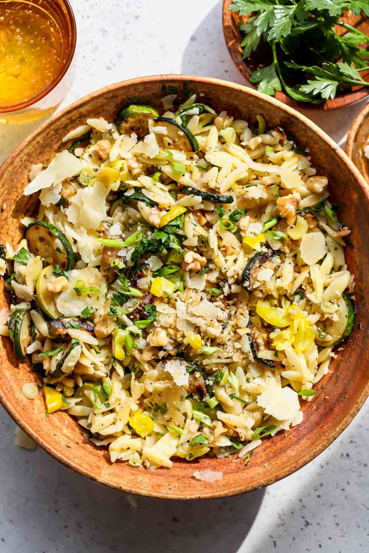 Zucchini orzo salad in a brown serving bowl topped with Parmesan and herbs