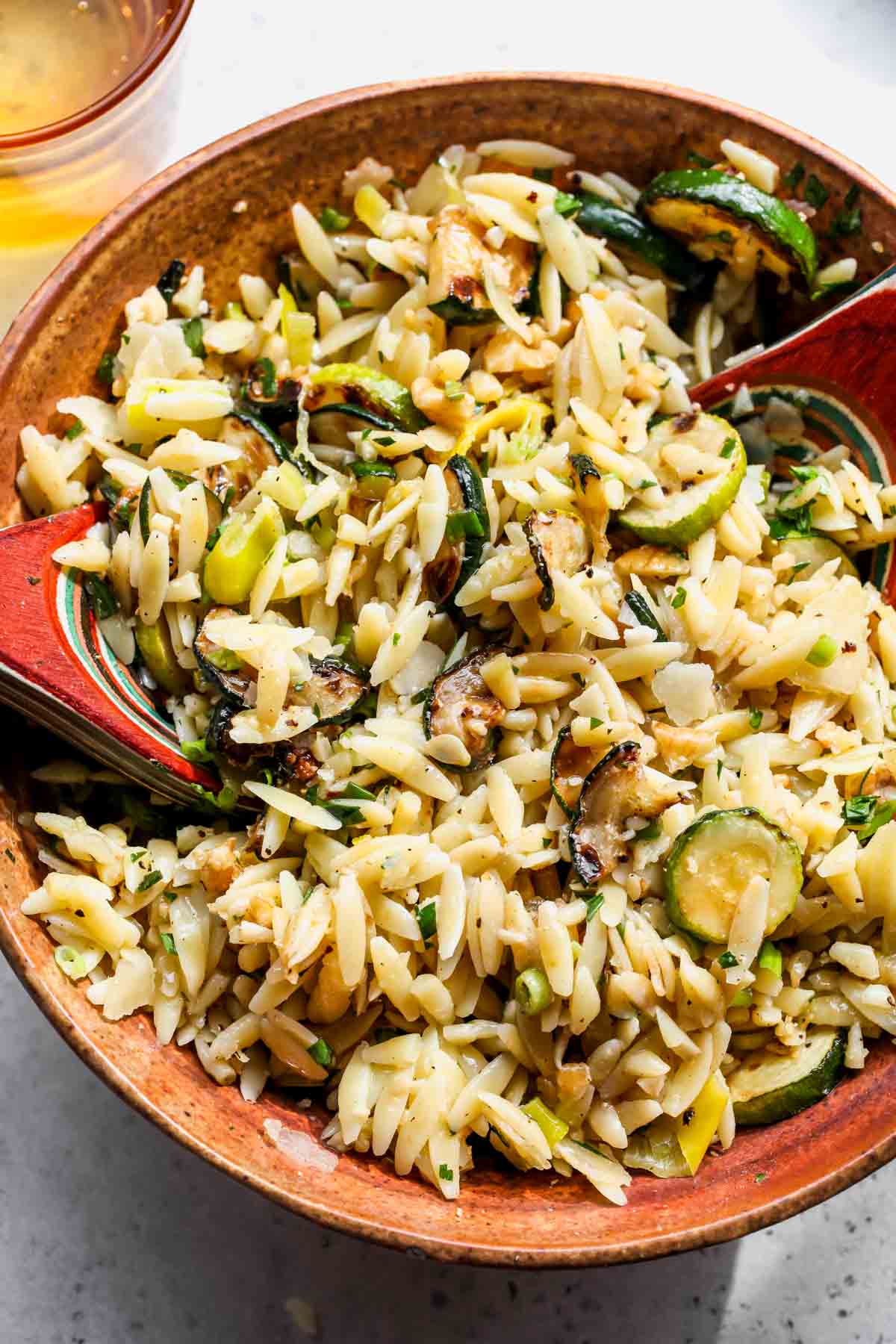 Salad spoons tossing zucchini orzo salad to mix ingredients