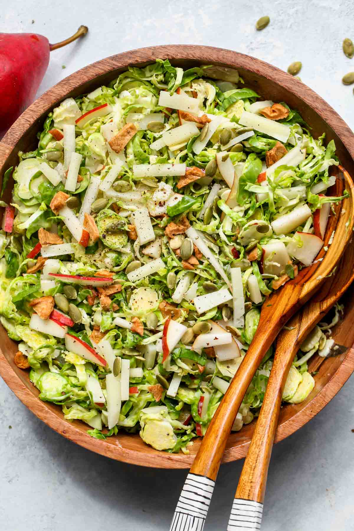 Thanksgiving shaved Brussels salad being mixed with pear, cheese, and pumpkin seeds in a wooden bowl.