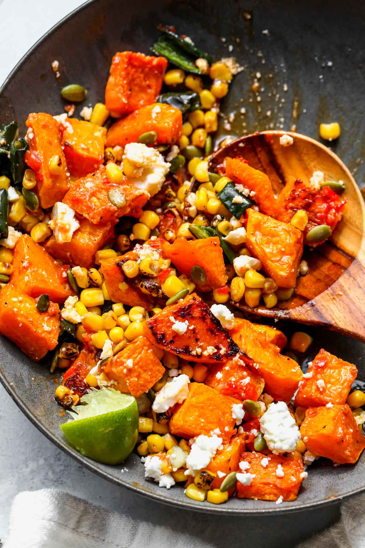 Roasted squash, poblano peppers, and corn being tossed in a serving bowl