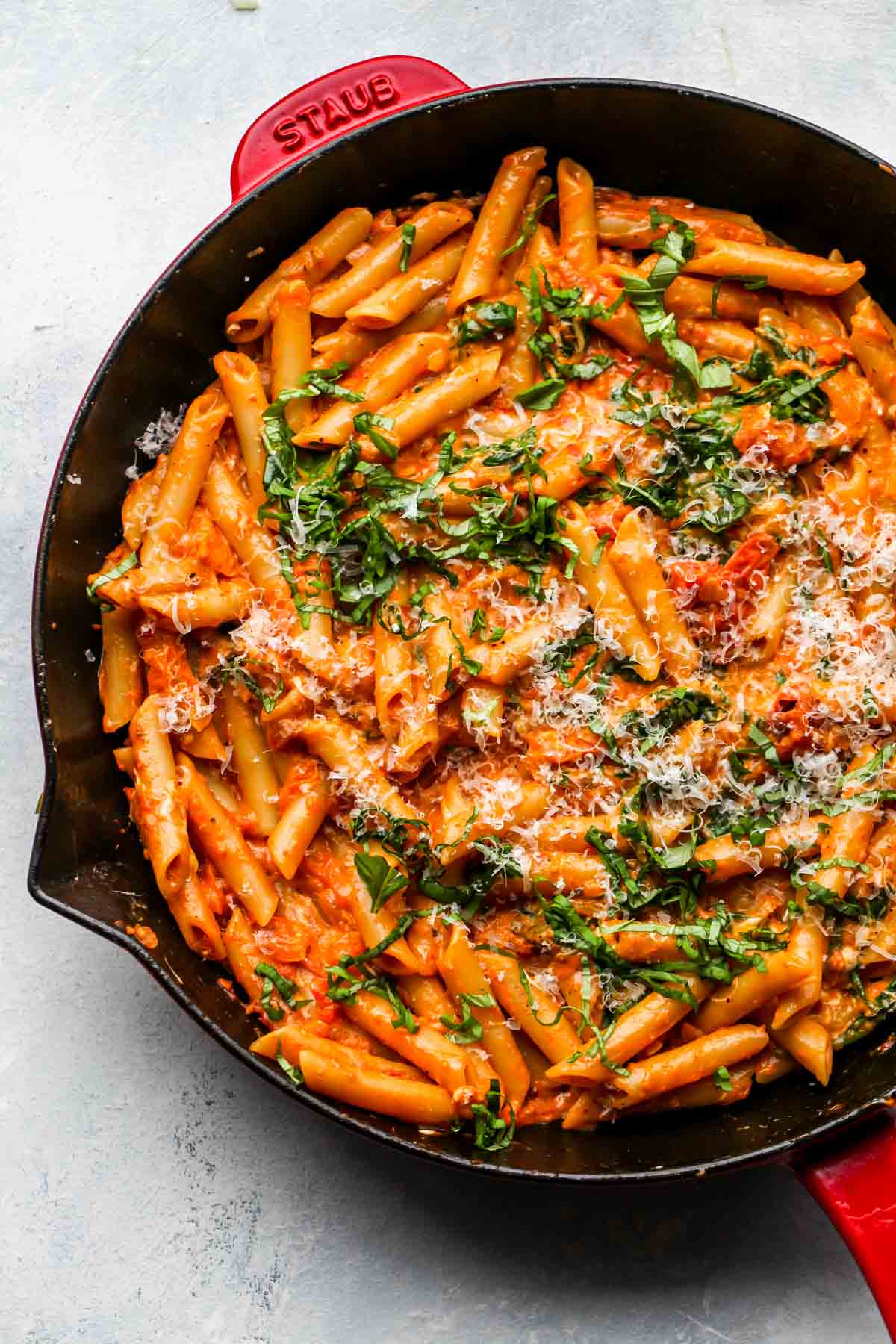 Cooked pasta being topped with basil and fresh Parmesan