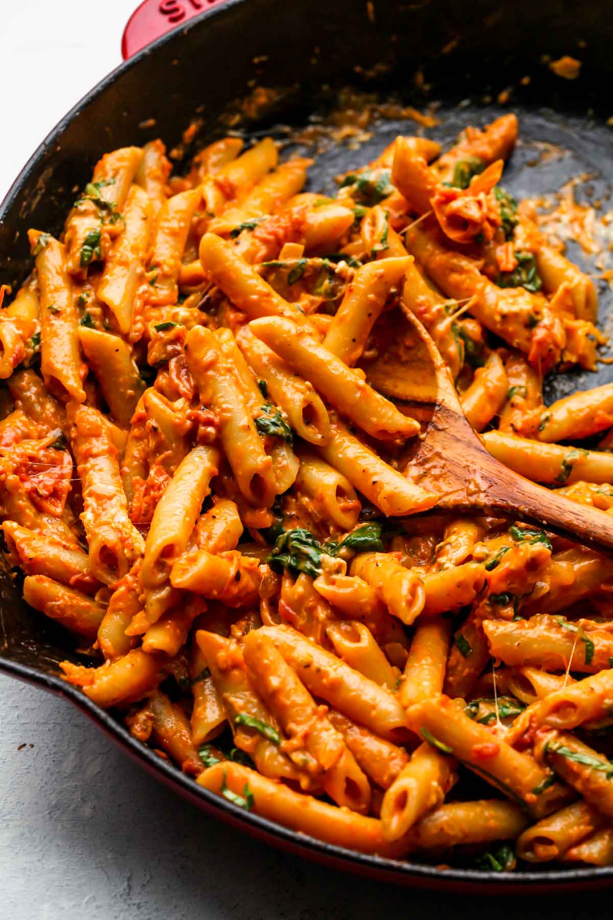 Creamy tomato pasta being stirred in a skillet