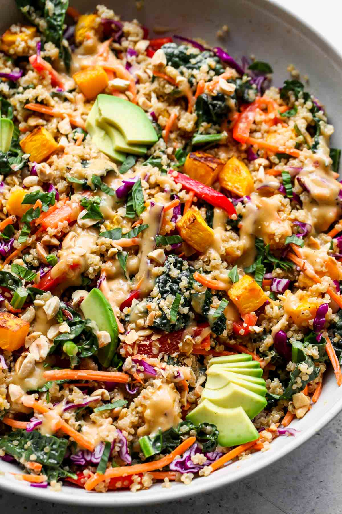 Butternut squash quinoa salad tossed with dressing in a white serving bowl