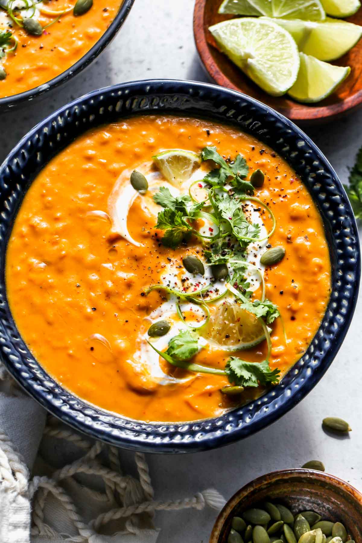 Blue bowl filled with pumpkin red lentil soup topped with herbs and pepitas