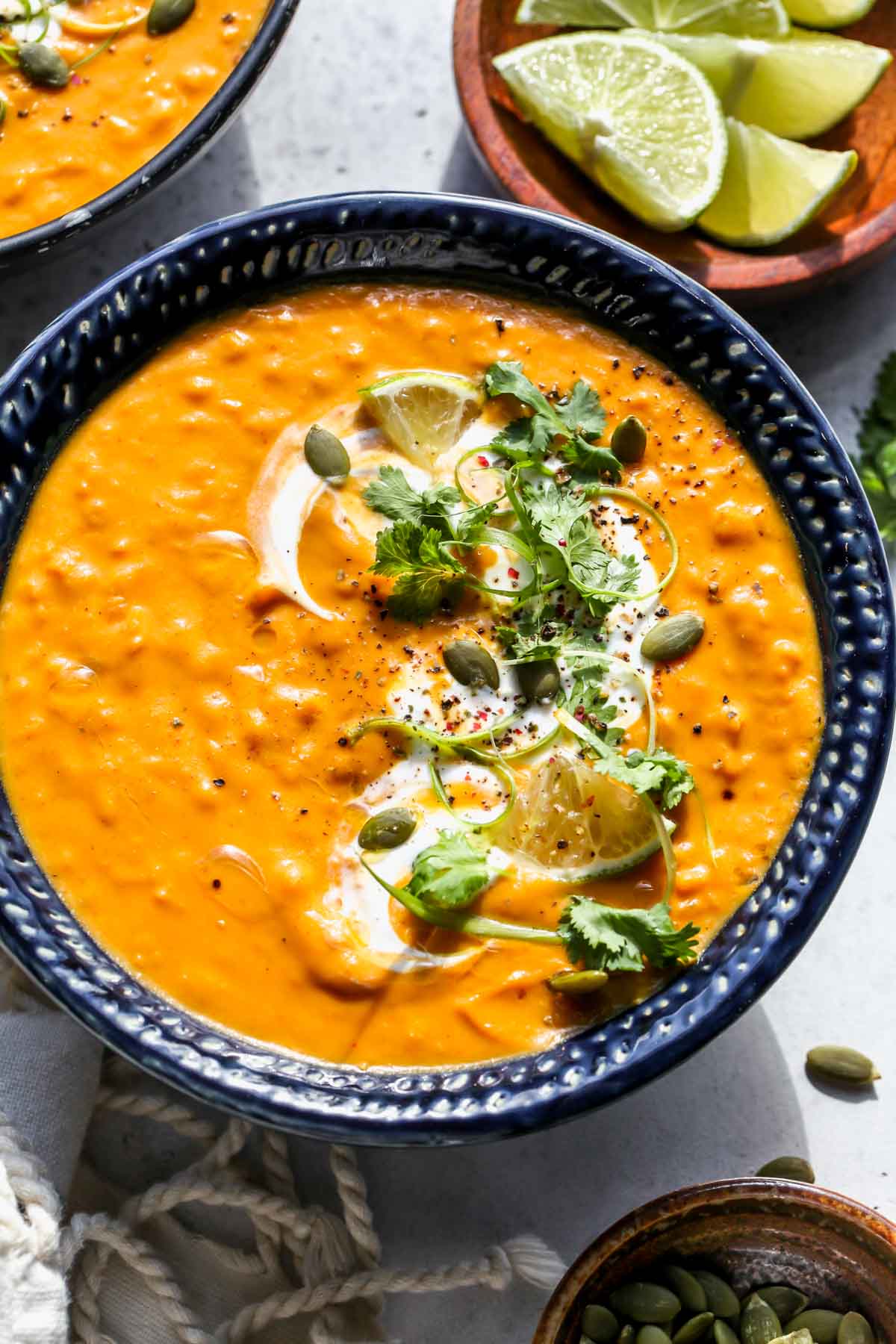 Serving of pumpkin lentil soup in a dark blue bowl with herb garnishes and yogurt swirl