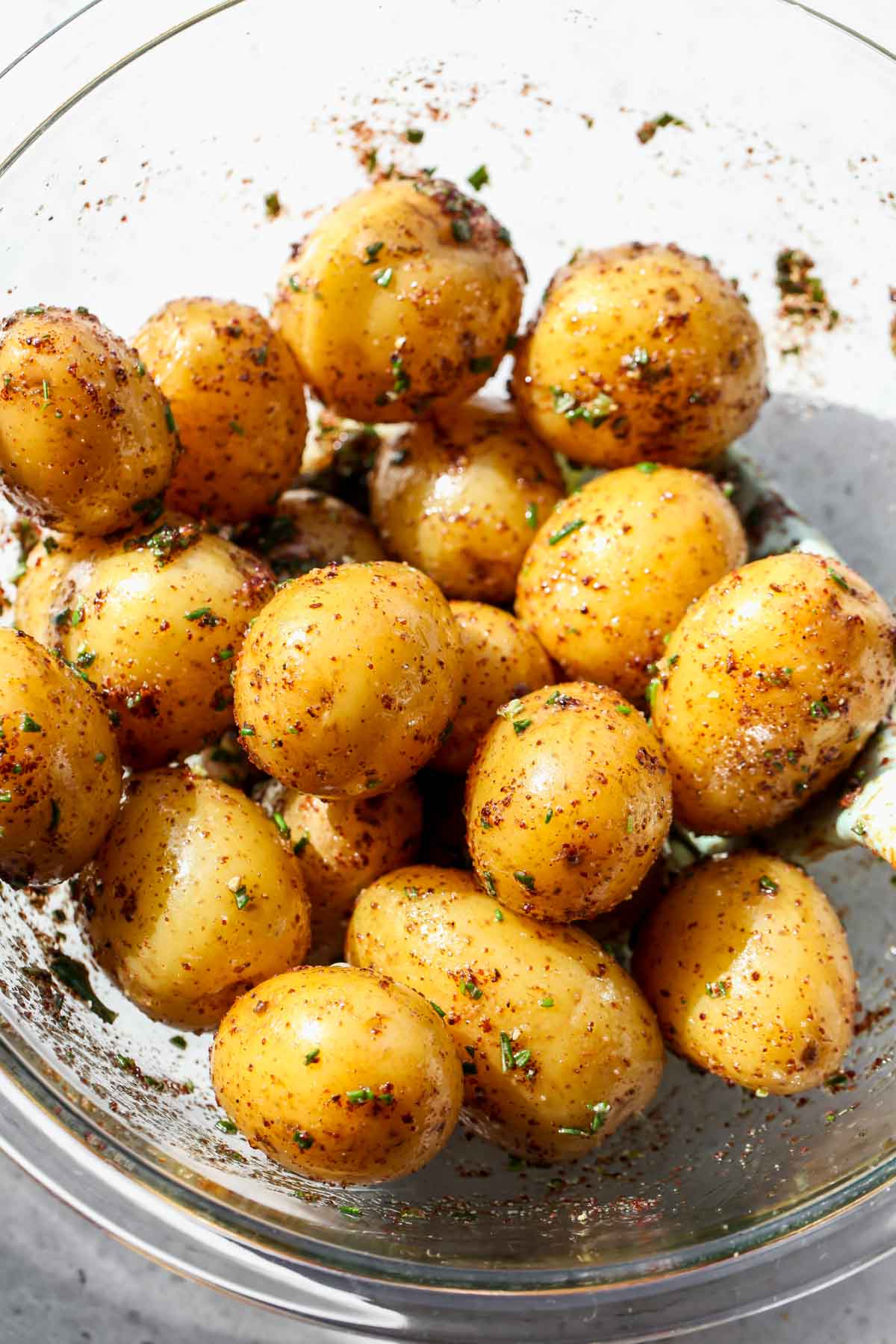 Small gold potatoes being tossed in oil and spices in a large bowl