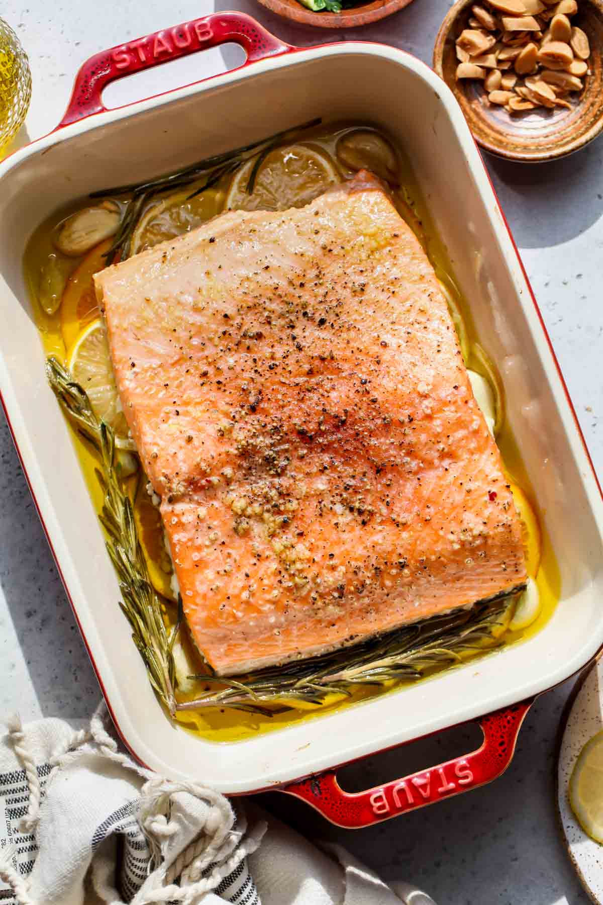 Piece of slow-roasted salmon in a pan surrounded by olive oil, citrus, and herbs