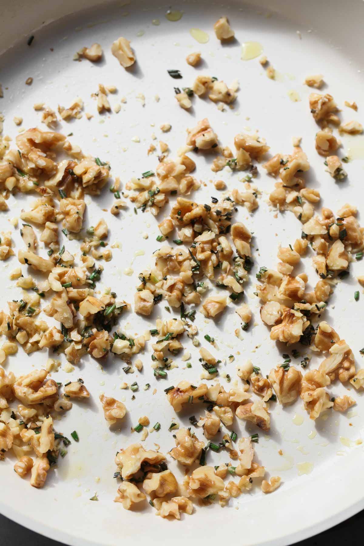 Rosemary walnuts being sautéed in a white skillet