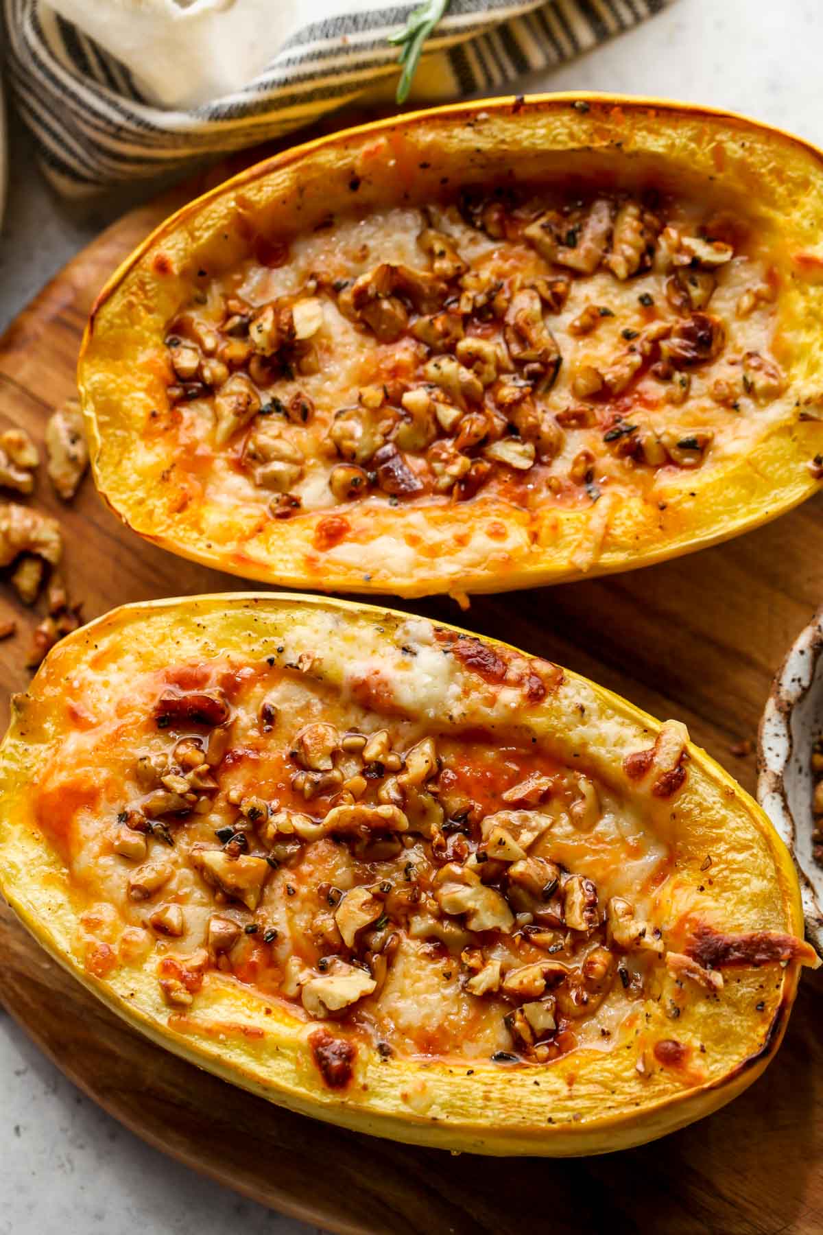 Pumpkin pasta sauce filled spaghetti squash topped with walnuts on a cutting board