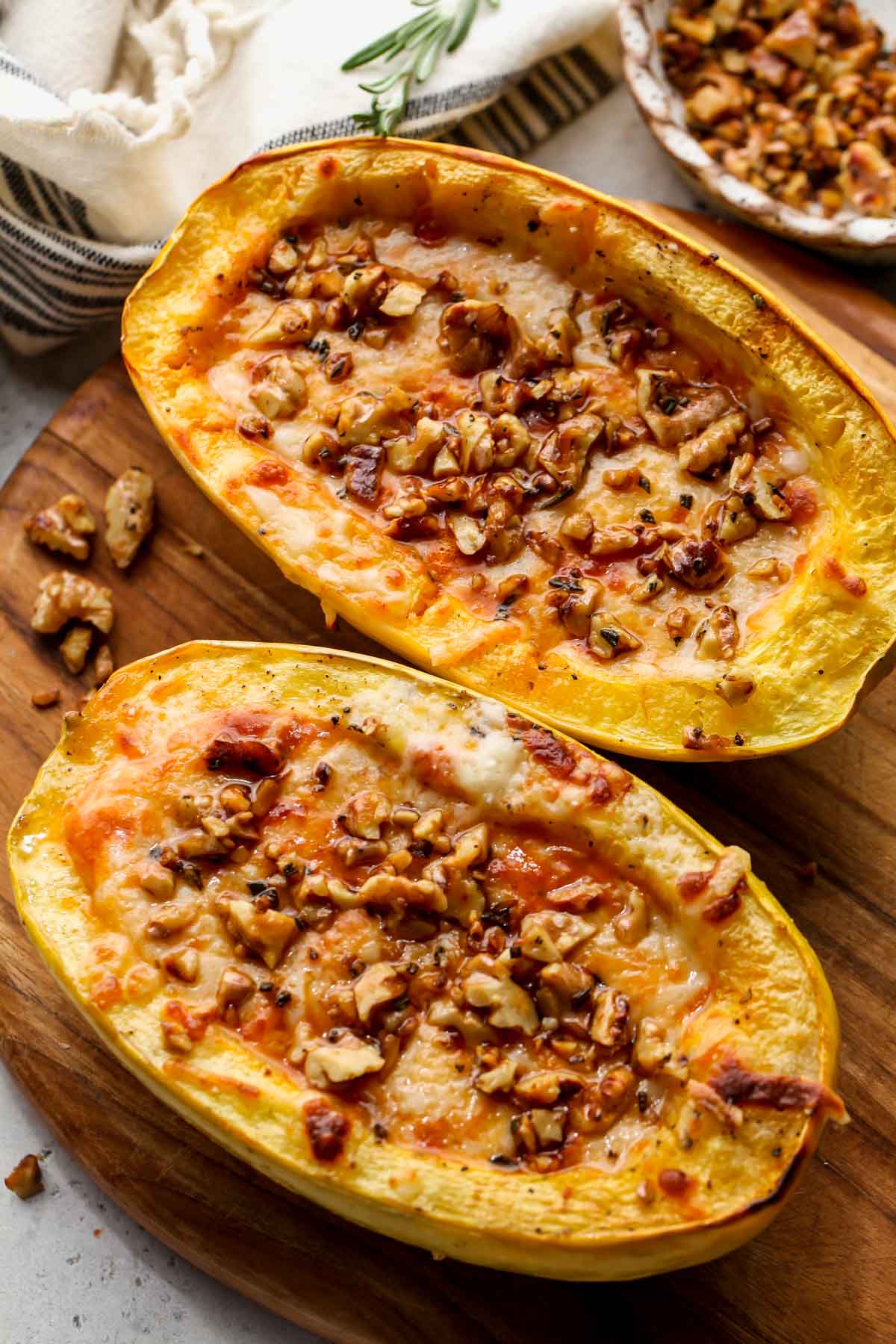 Spaghetti squash filled with pumpkin pasta sauce and topped with walnuts on a wooden cutting board