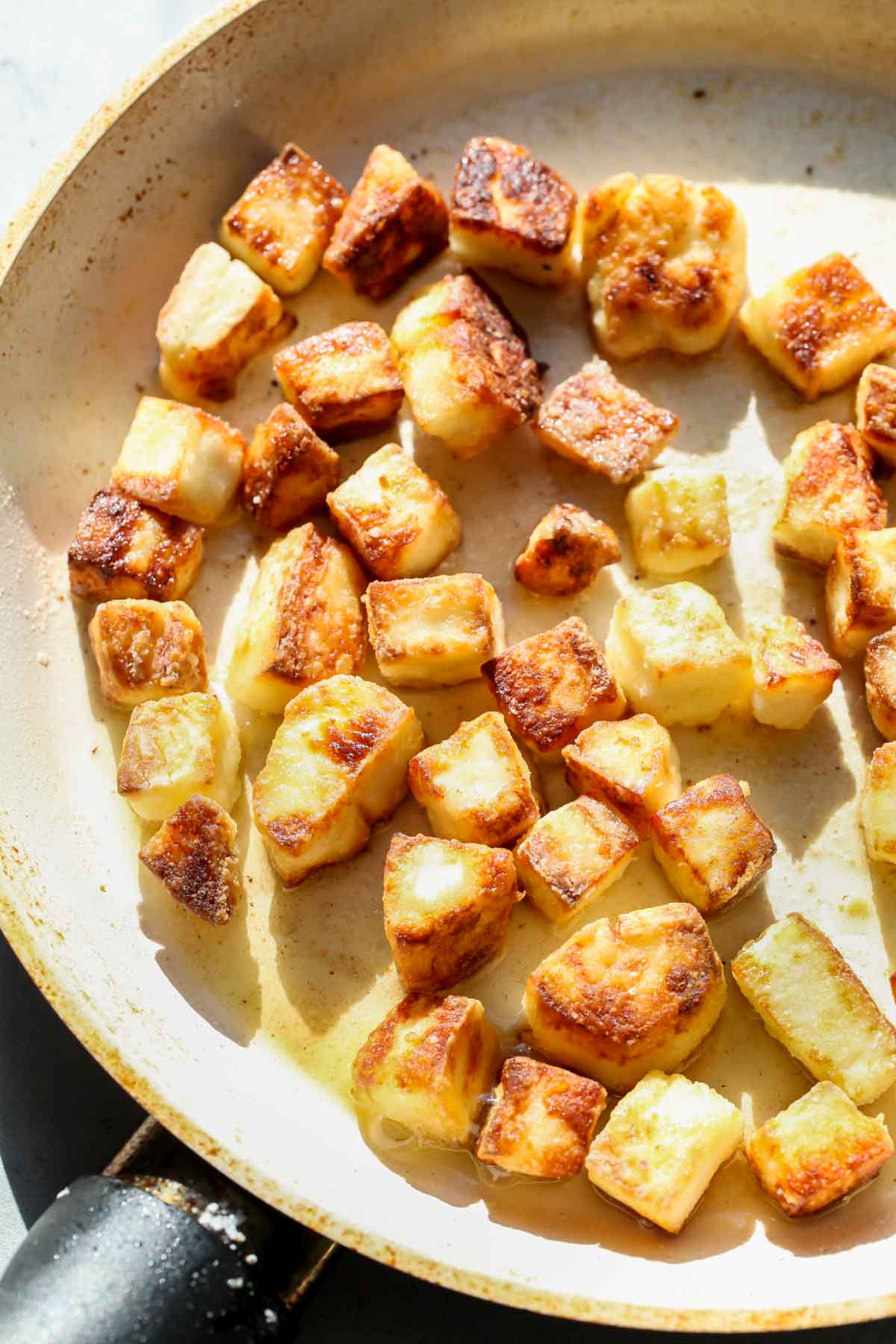 Halloumi croutons being fried in a white skillet