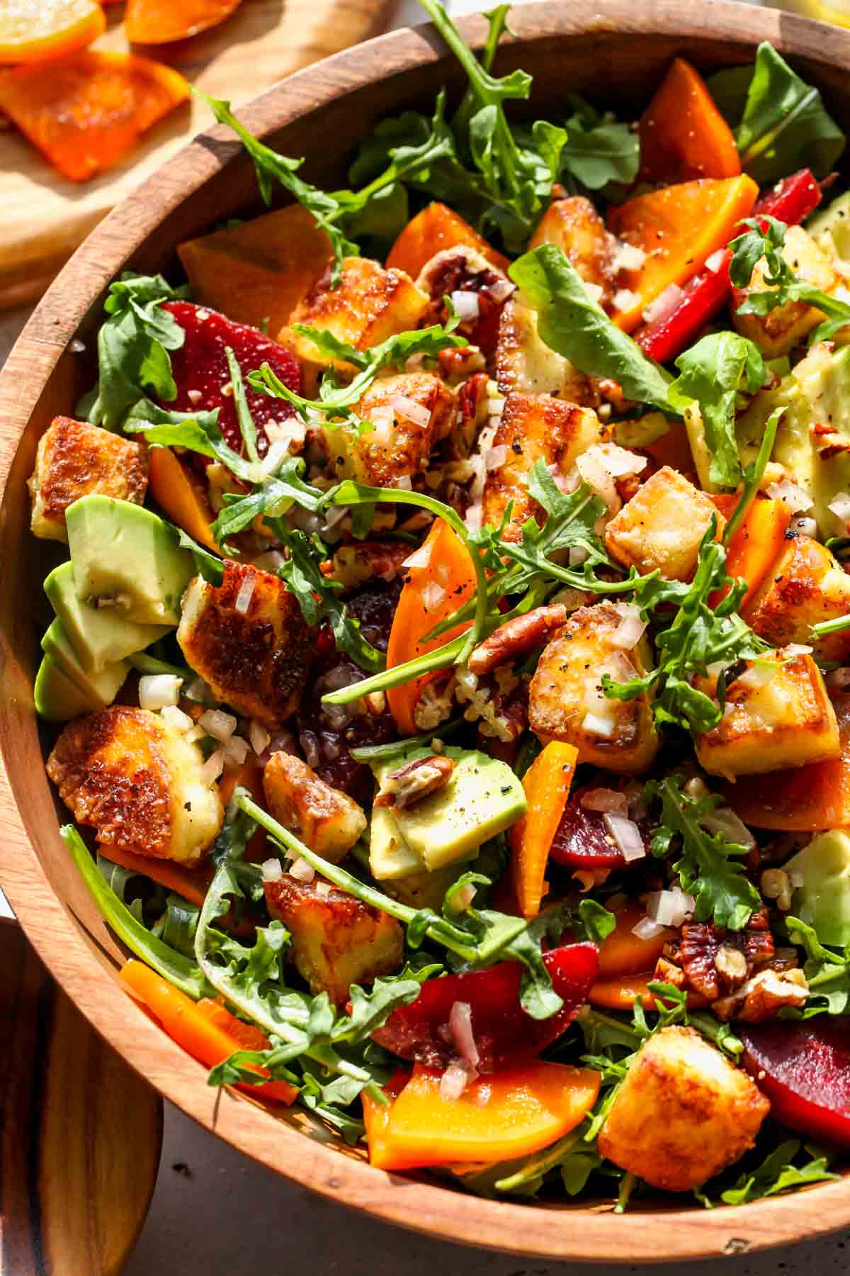 Arugula and persimmon salad being tossed in a bowl