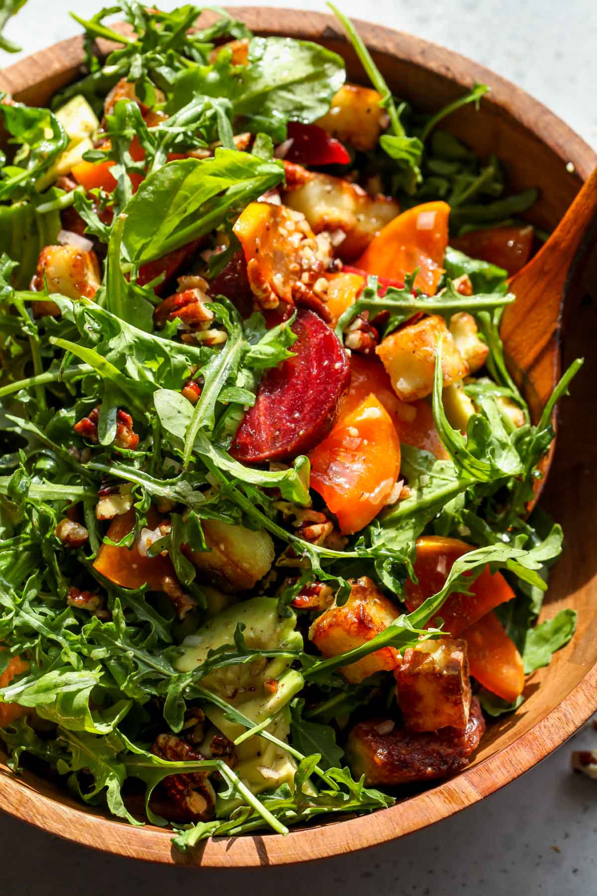 Arugula salad being tossed with wooden serving utensils