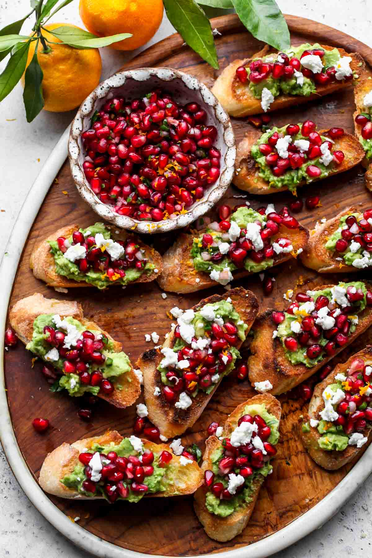 Wooden serving platter topped with crostinis and pomegranate salsa