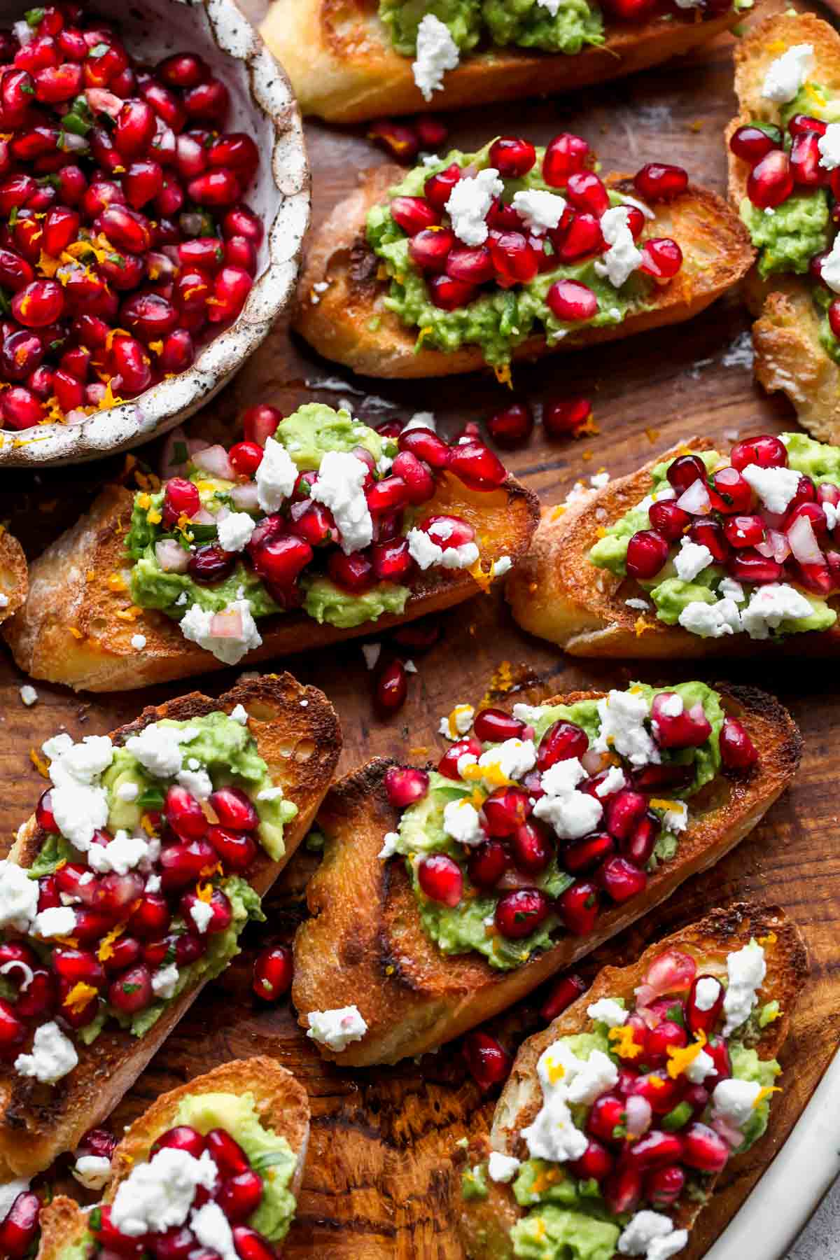 Mini avocado toasts on a wooden serving board topped with pomegranate salsa
