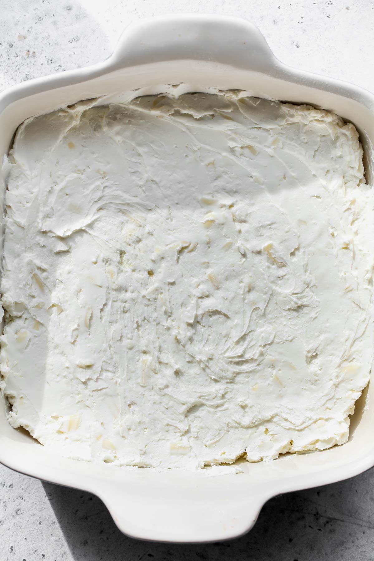 Goat cheese mixture being spread in a square baking dish.