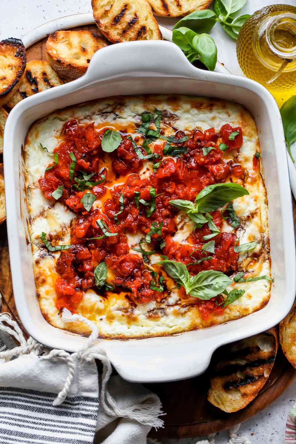 Baked goat cheese dip topped with bruschetta and basil surrounded by grilled bread.
