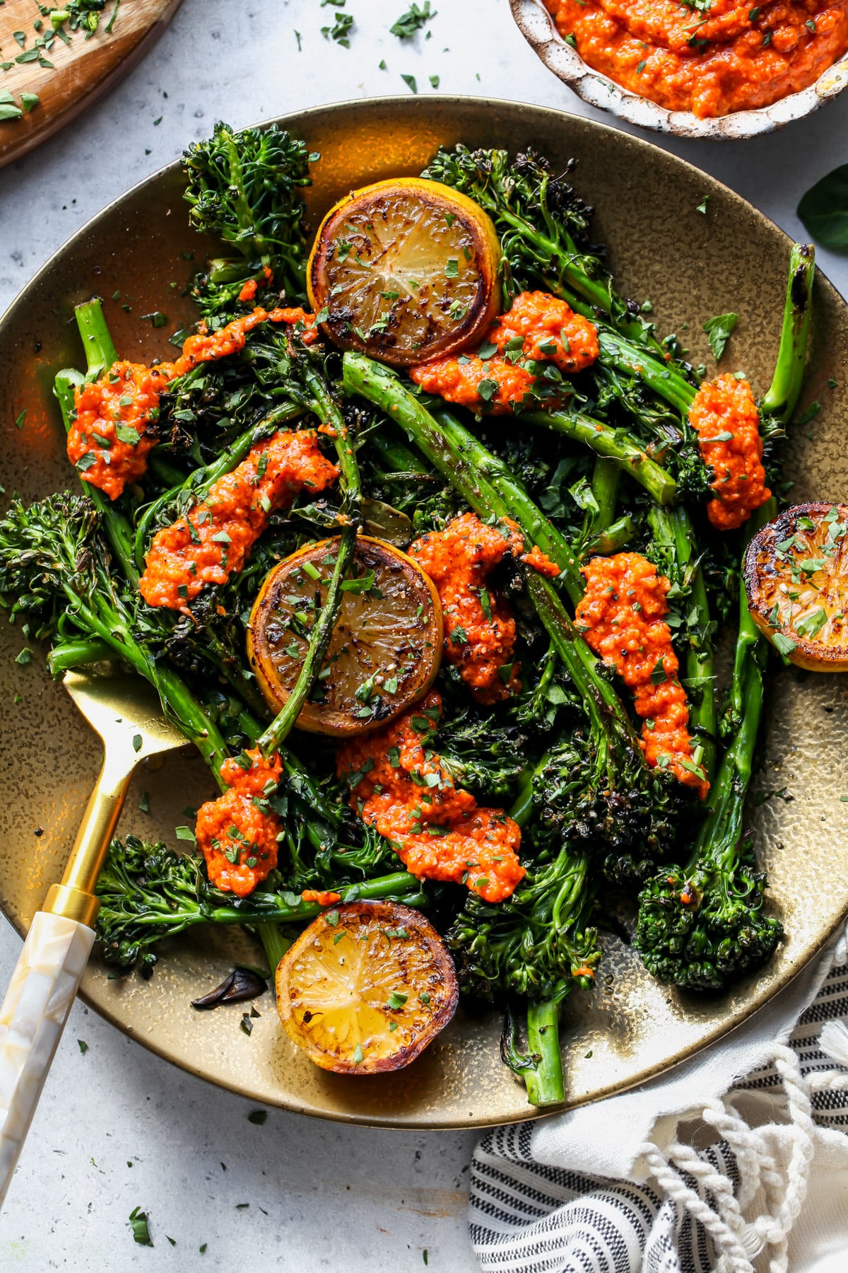 Charred baby broccoli on a gold plate with hazelnut romesco spooned overtop