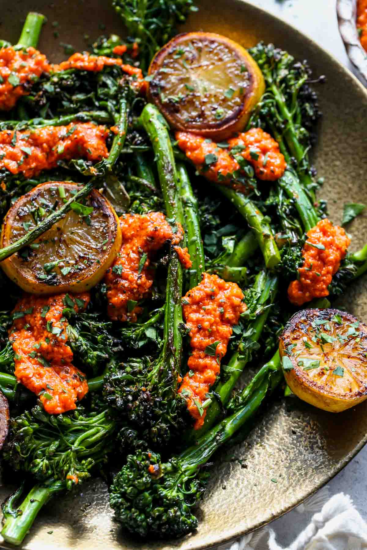 Baby broccoli arranged on a serving platter with romesco sauce and lemon slices