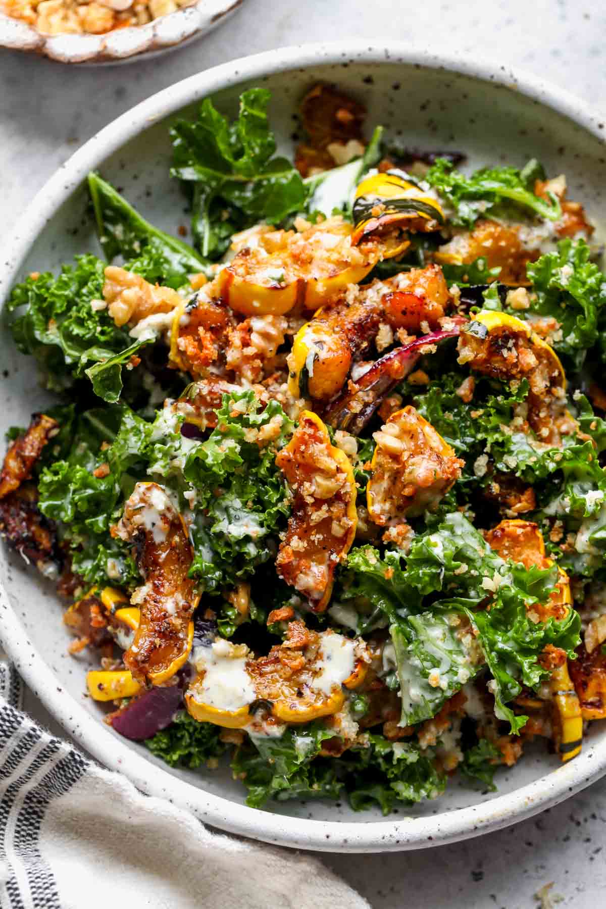 A white serving bowl filled with roasted squash and kale salad and drizzled with creamy dressing