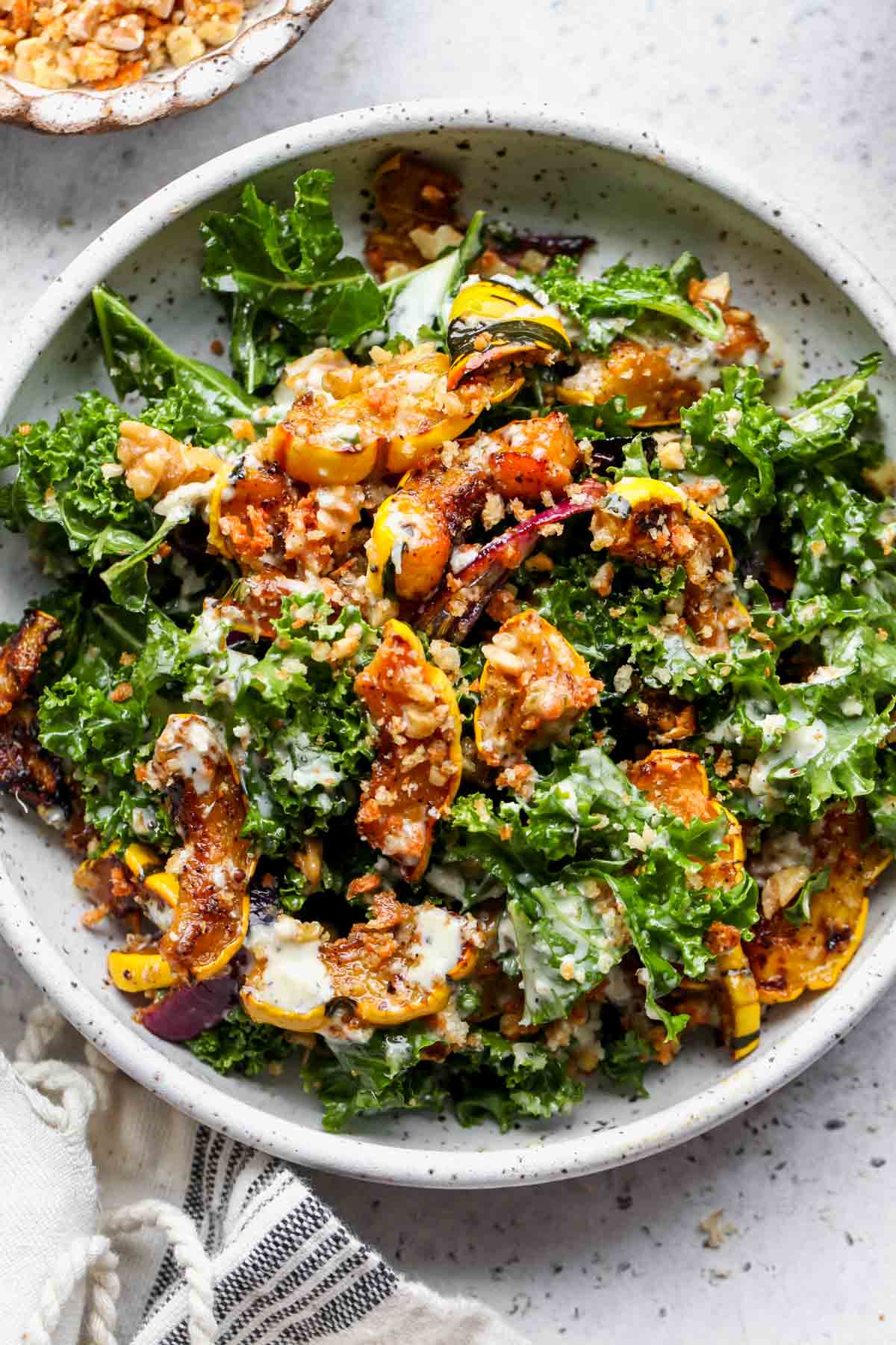 White speckled bowl filled with roasted squash salad on a gray surface
