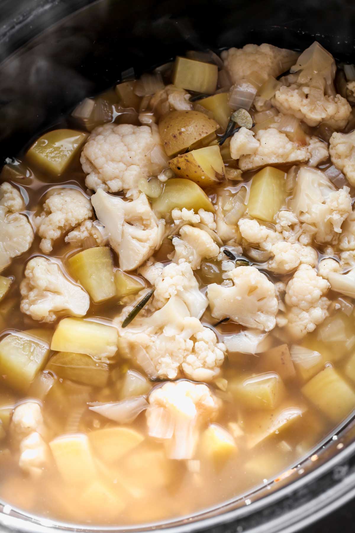 Cauliflower, potatoes, broth, and rosemary cooking in a crock pot