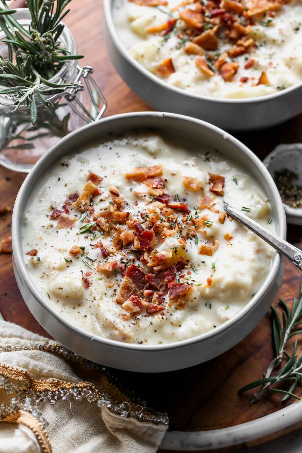 Two grey bowls filled with rosemary potato soup on a wooden serving platter