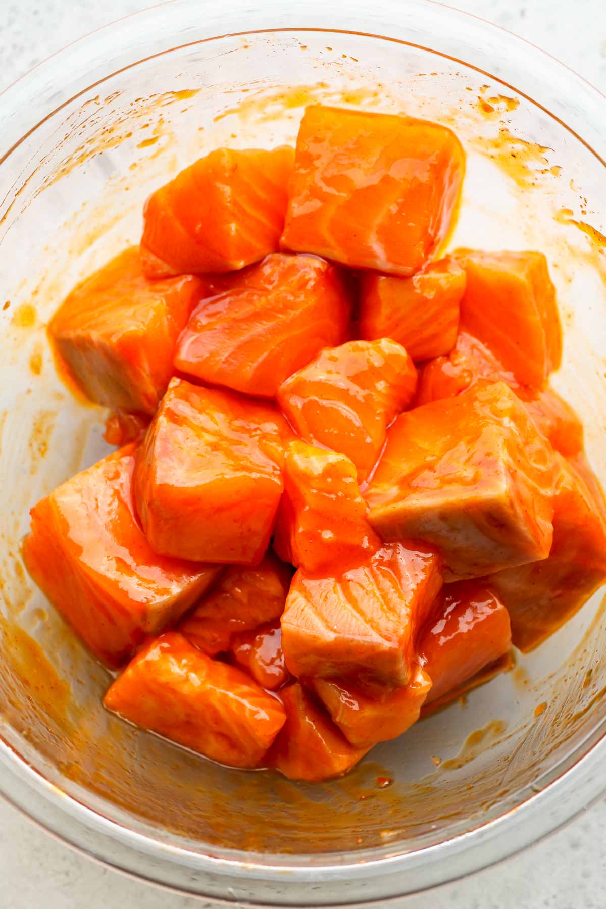Cubes of salmon being tossed in honey-gochujang mixture in a clear bowl