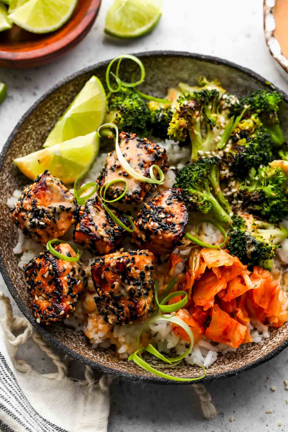 Sesame crusted salmon bowl being assembled in a rustic bowl and drizzled with sauce