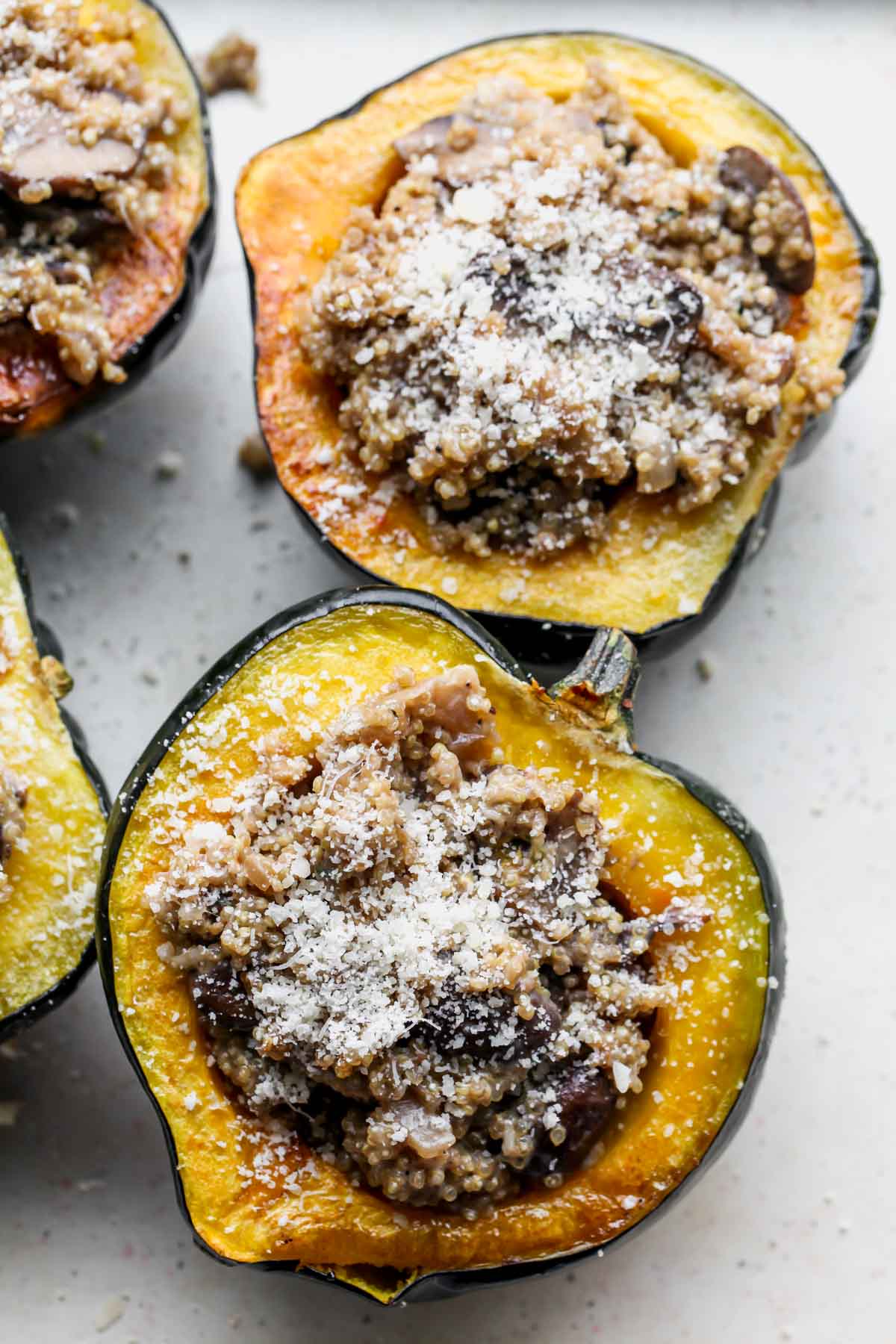 Acorn squashes being stuffed with quinoa mixture and topped with parmesan cheese