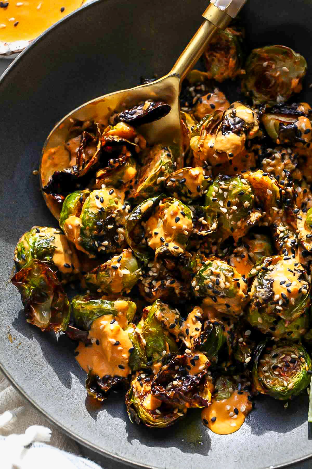 Crispy Brussels sprouts tossed with kimchi sauce in a dark serving bowl
