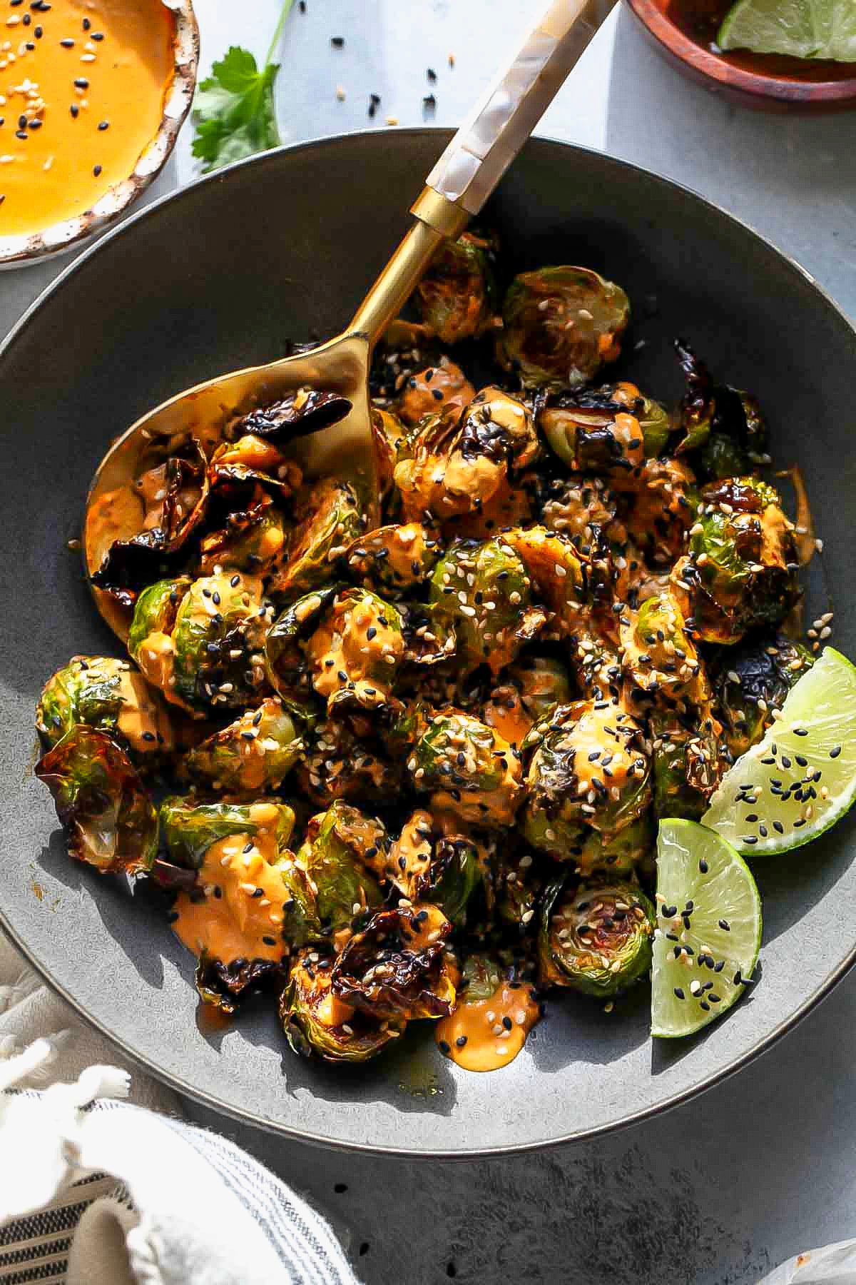 Dark serving bowl filled with crispy Brussels tossed in a sauce