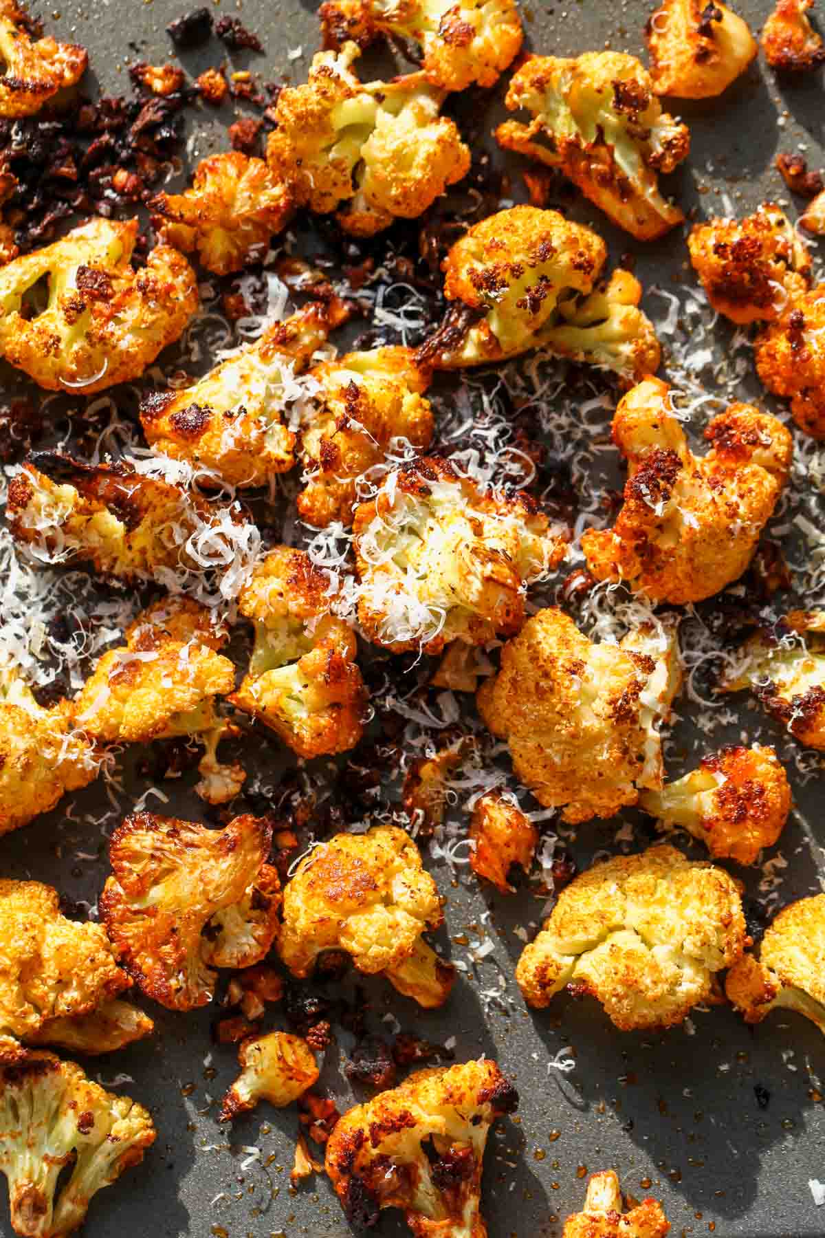 Cauliflower florets being roasted on a sheet pan and topped with grated Parmesan cheese.