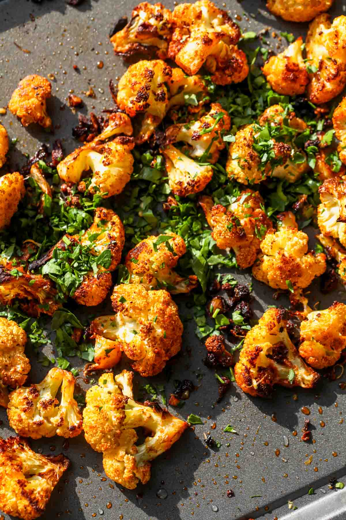 Parsley being scattered over cauliflower florets on a baking sheet.