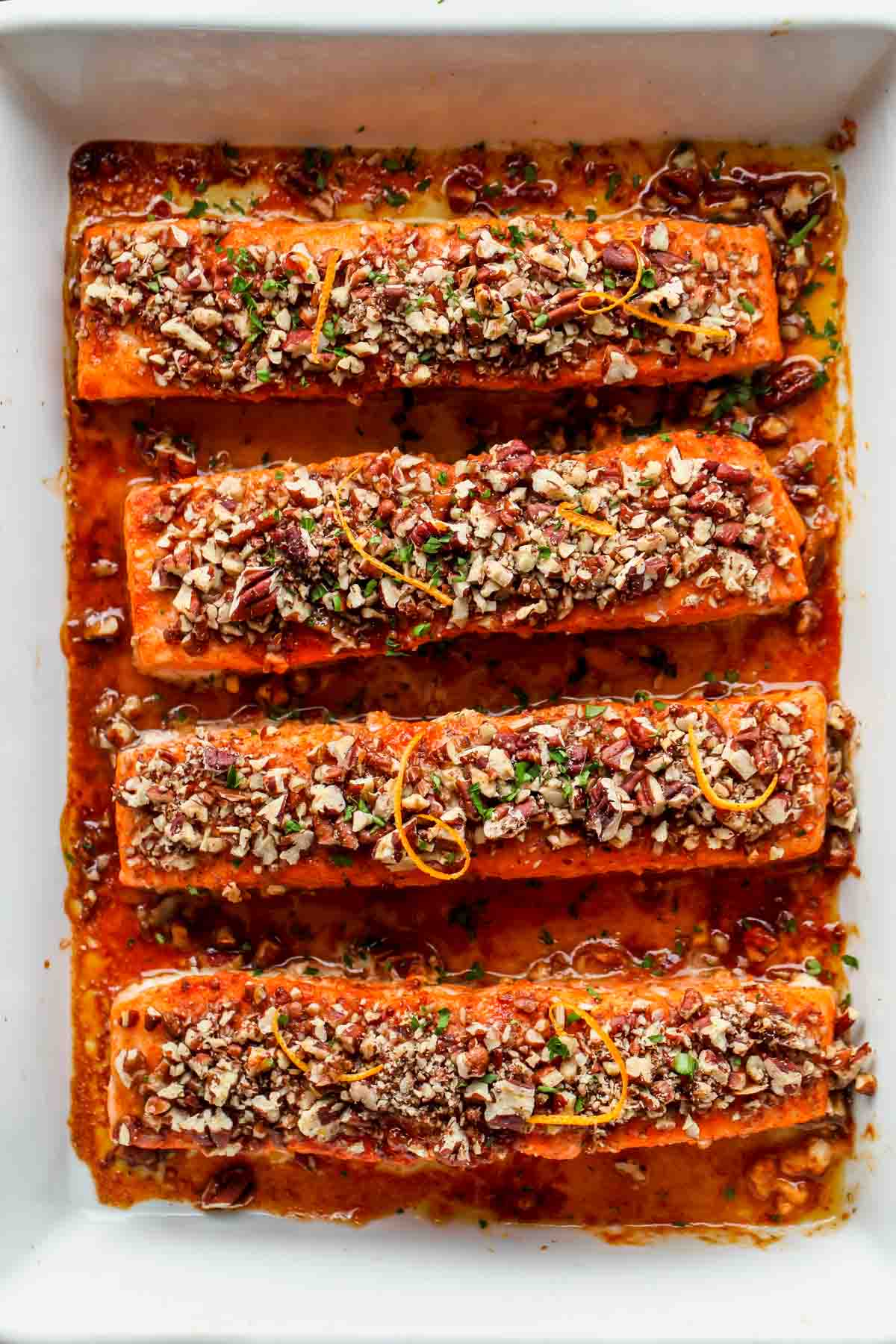 orange maple glazed salmon topped with crushed pecans arranged in a white baking dish