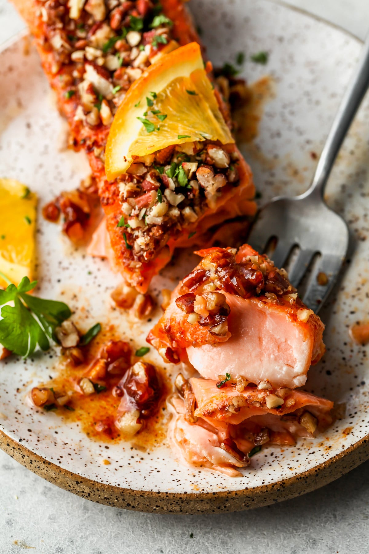 A fork taking a bite out of maple glazed salmon fillet on a white plate