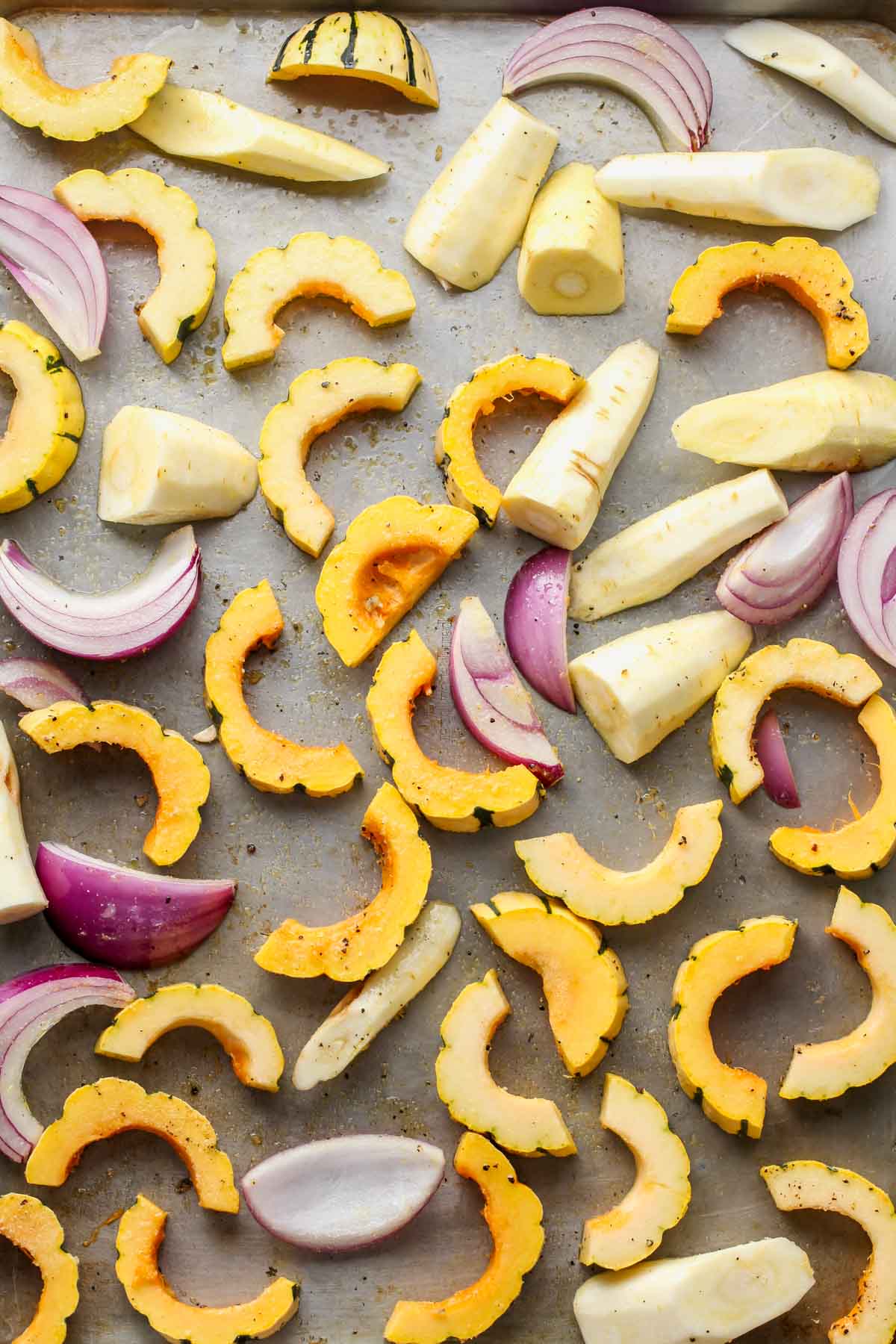 Squash, red onion, and parsnips arranged on a baking sheet