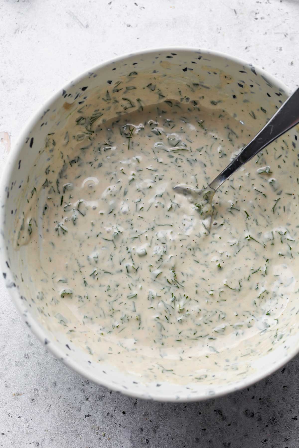 Herby tahini sauce being mixed in a white speckled bowl