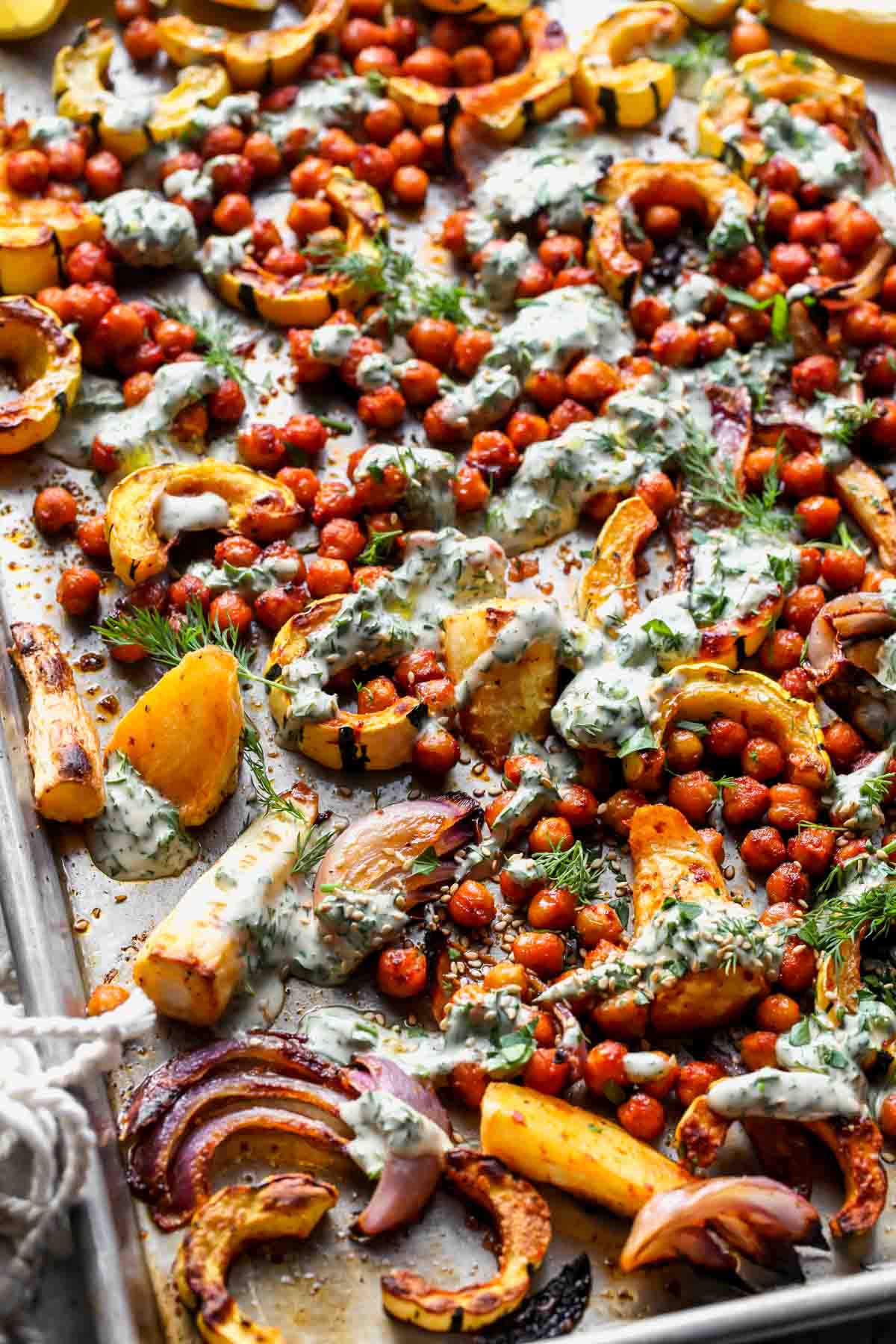 Sheet Pan Vegetable Bake drizzled with tahini sauce and garnished with fresh herbs
