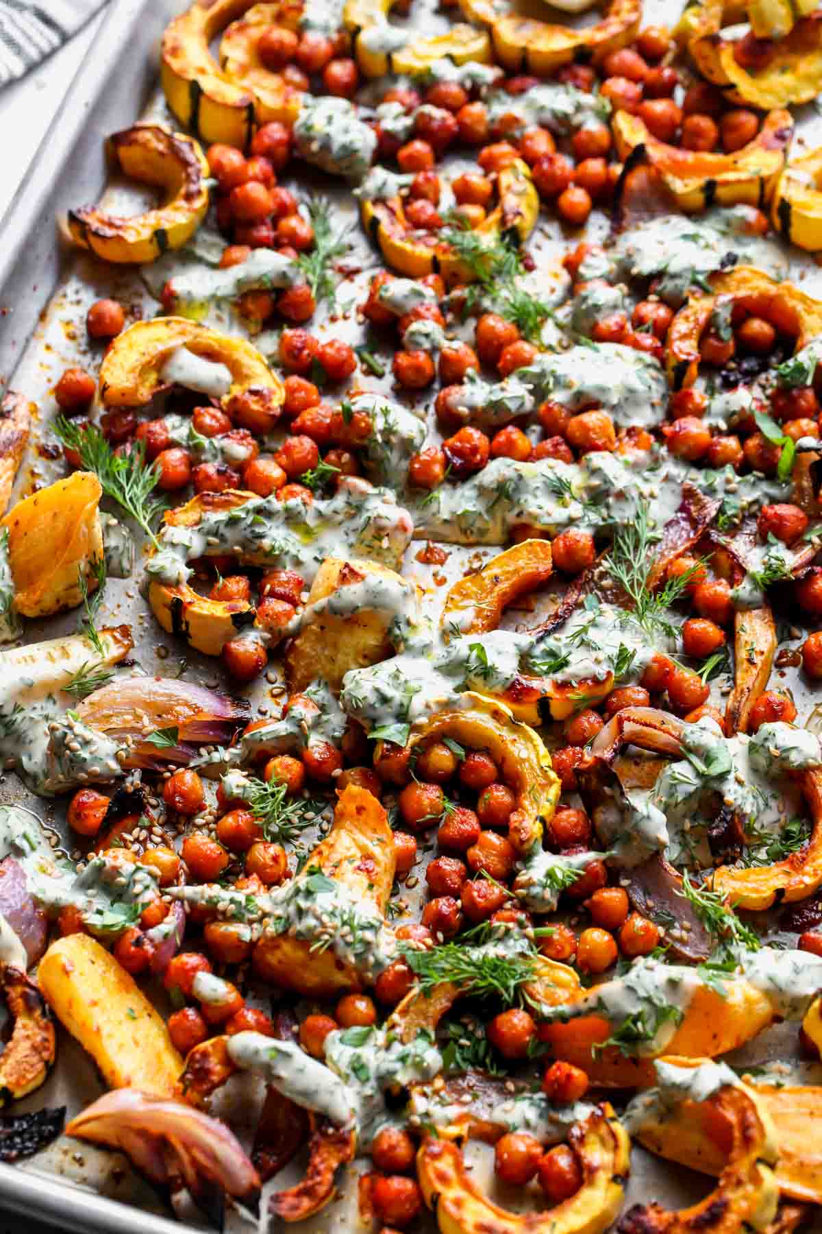 Sheet pan vegetable and chickpea bake on a rimmed baking sheet drizzled with tahini sauce