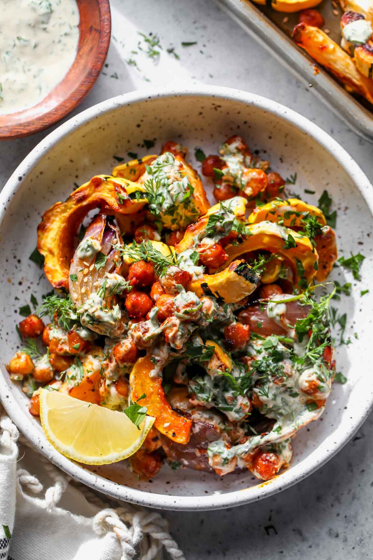 White bowl filled with roasted veggies, chickpeas, and tahini sauce