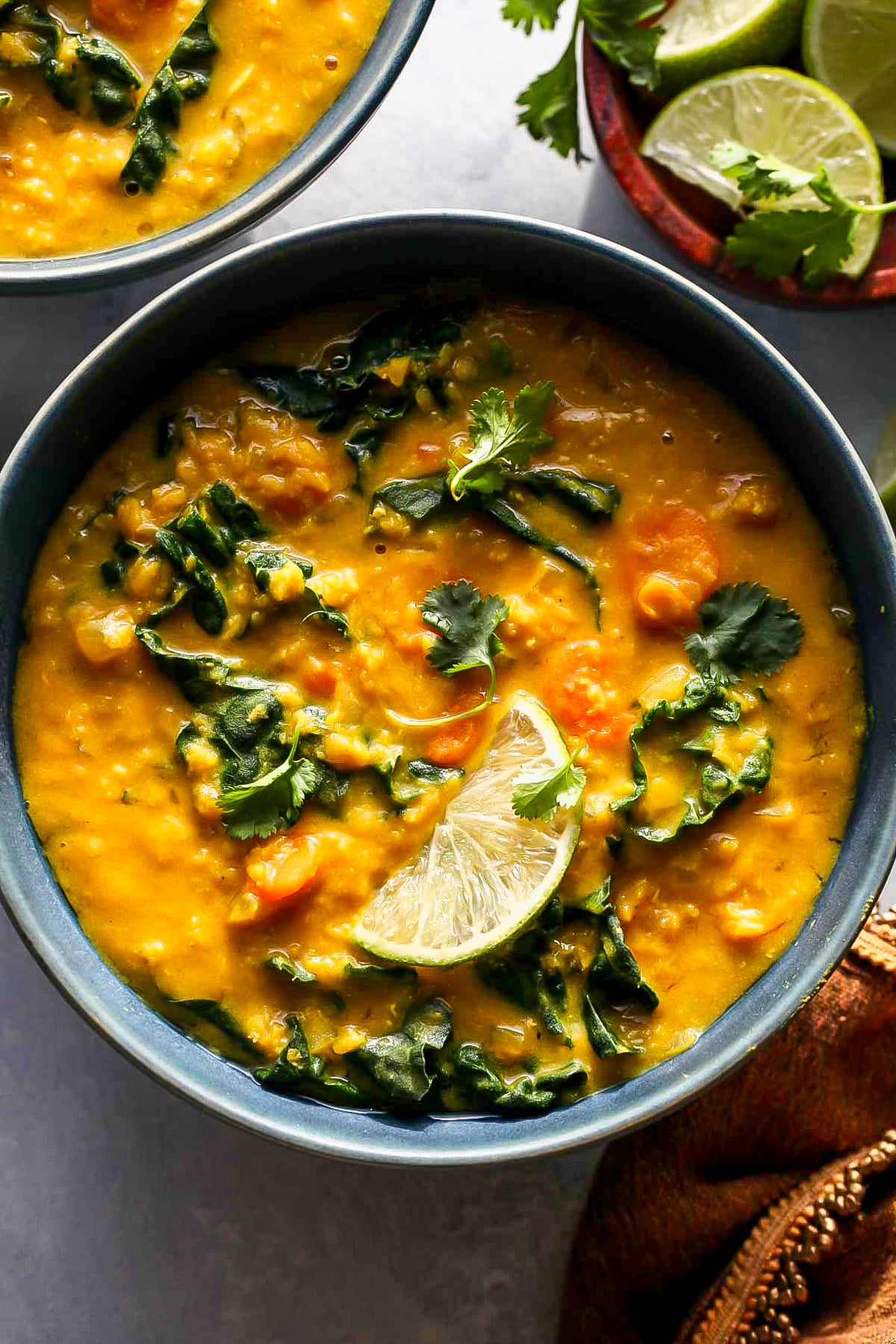 Slow cooker lentil soup in a blue bowl topped with a wedge of lime and cilantro