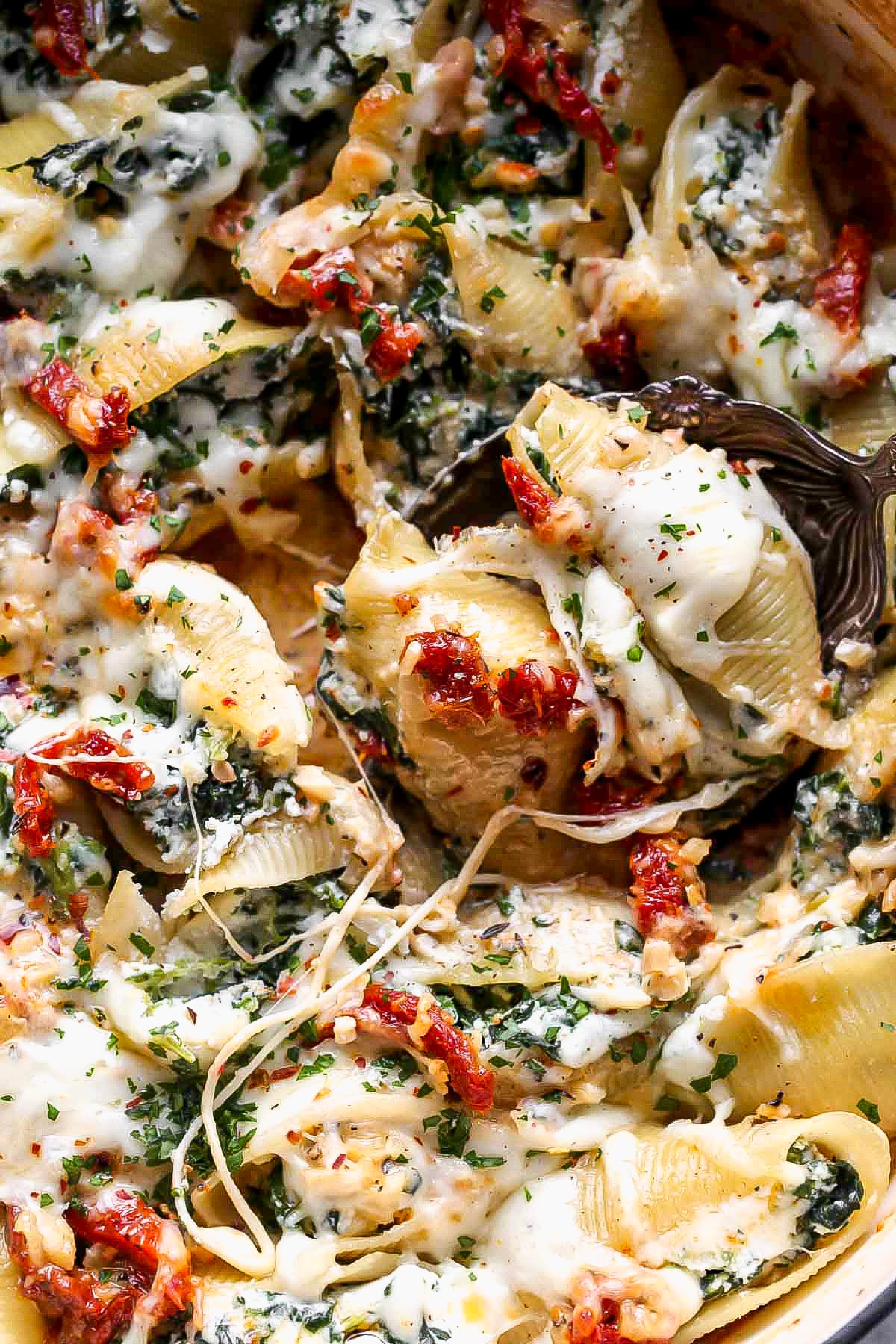 Ricotta stuffed shells being lifted out of the pan by a golden serving spoon