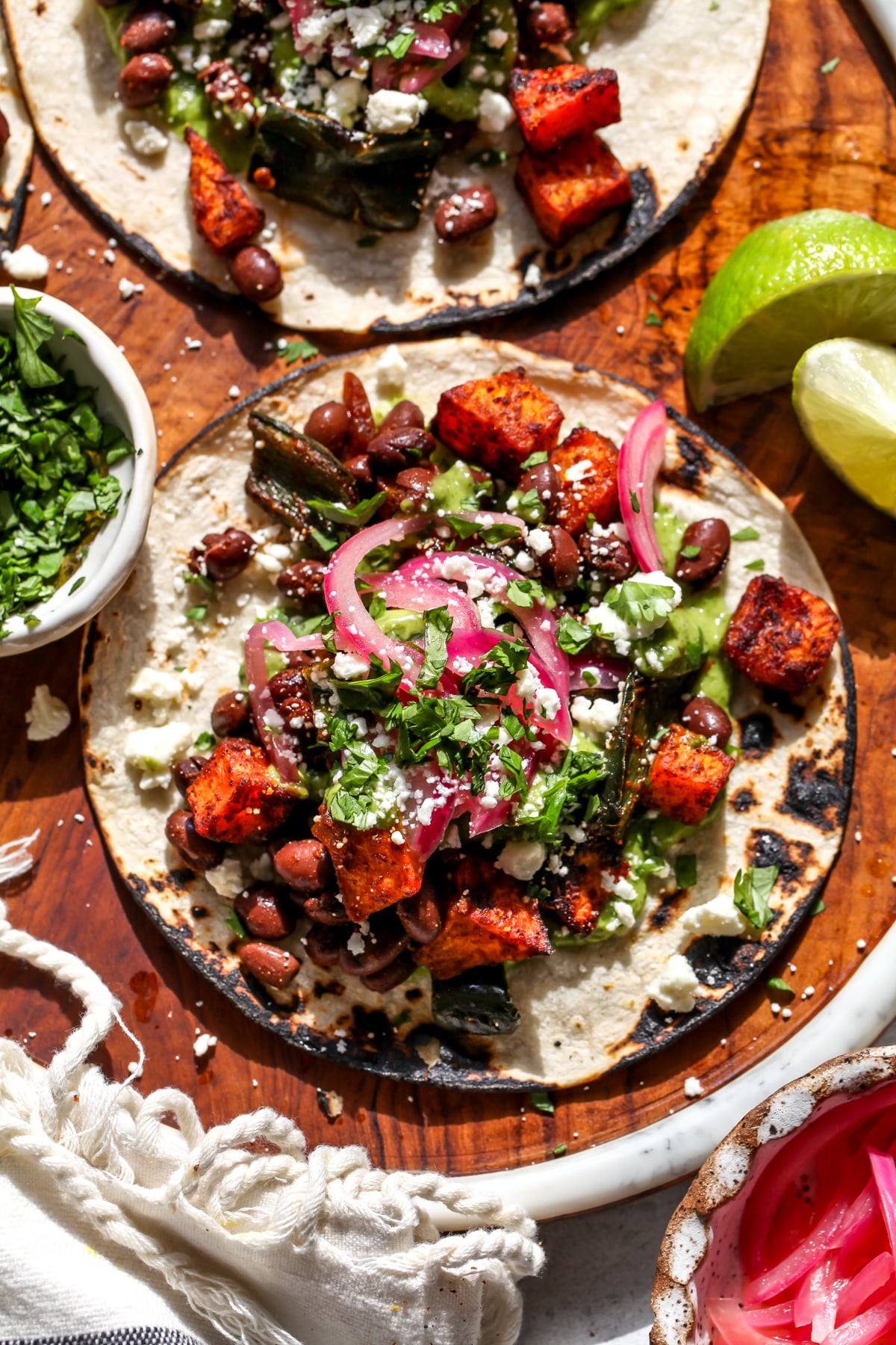 Butternut squash tacos styled on a wooden platter topped with picked onion, cotija cheese, and cilantro.