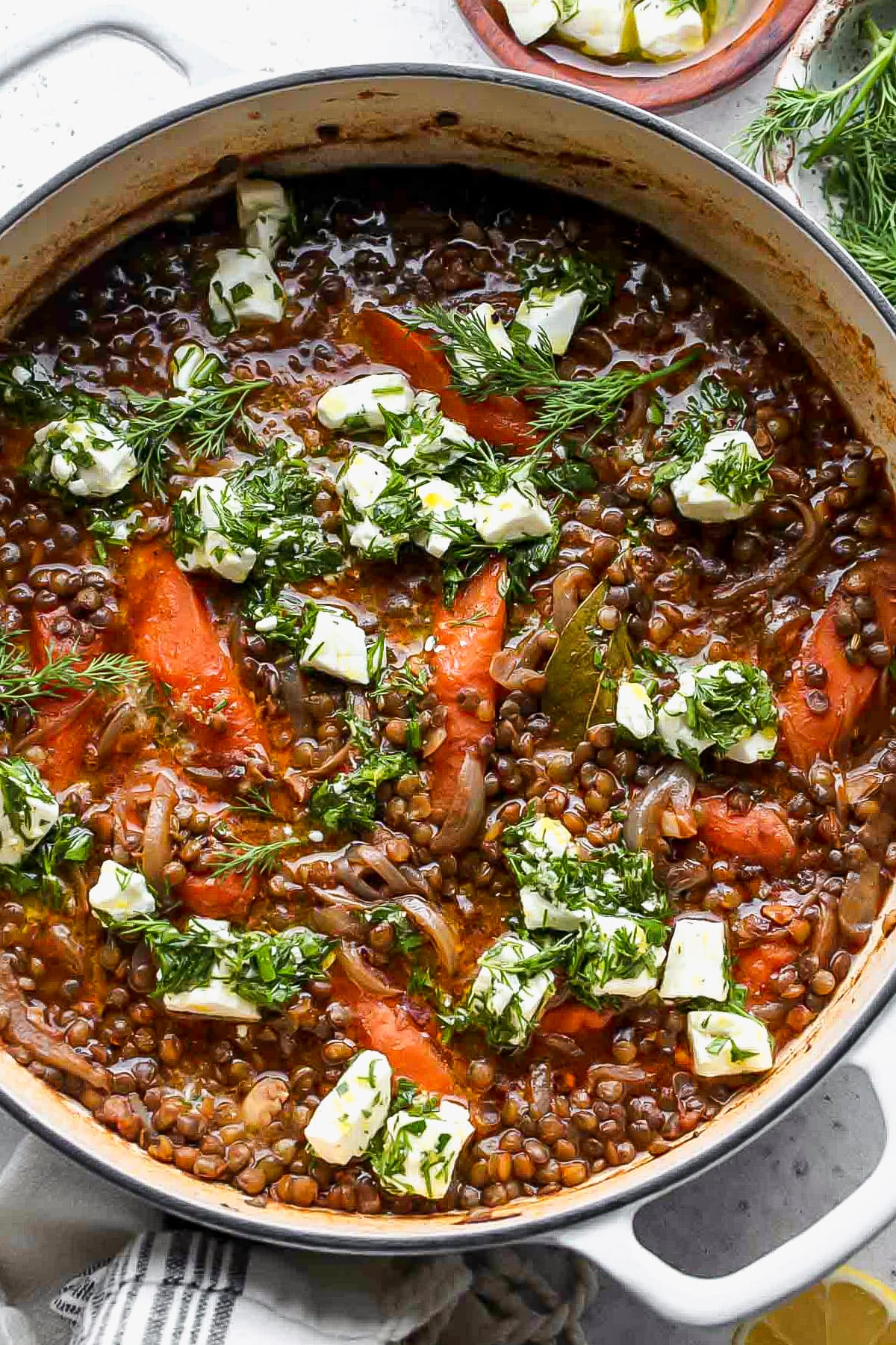 Stewed lentils in a pot topped with chunks of marinated feta and herbs