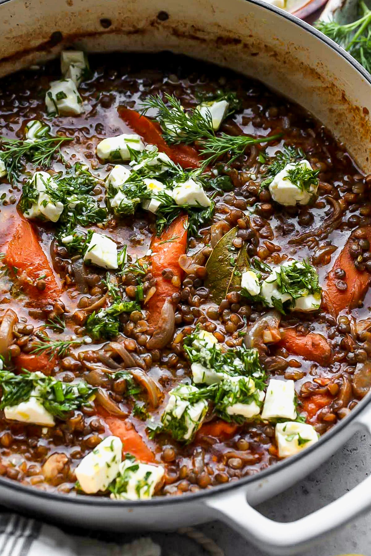 Marinated feta being dolloped over a pot of simmered lentils and carrots