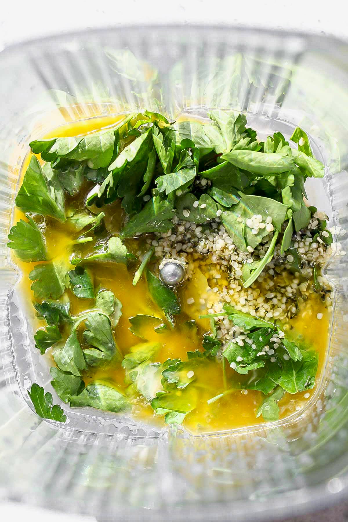 Parsley, lemon, olive oil, hemp seeds, and tahini being added to a blender