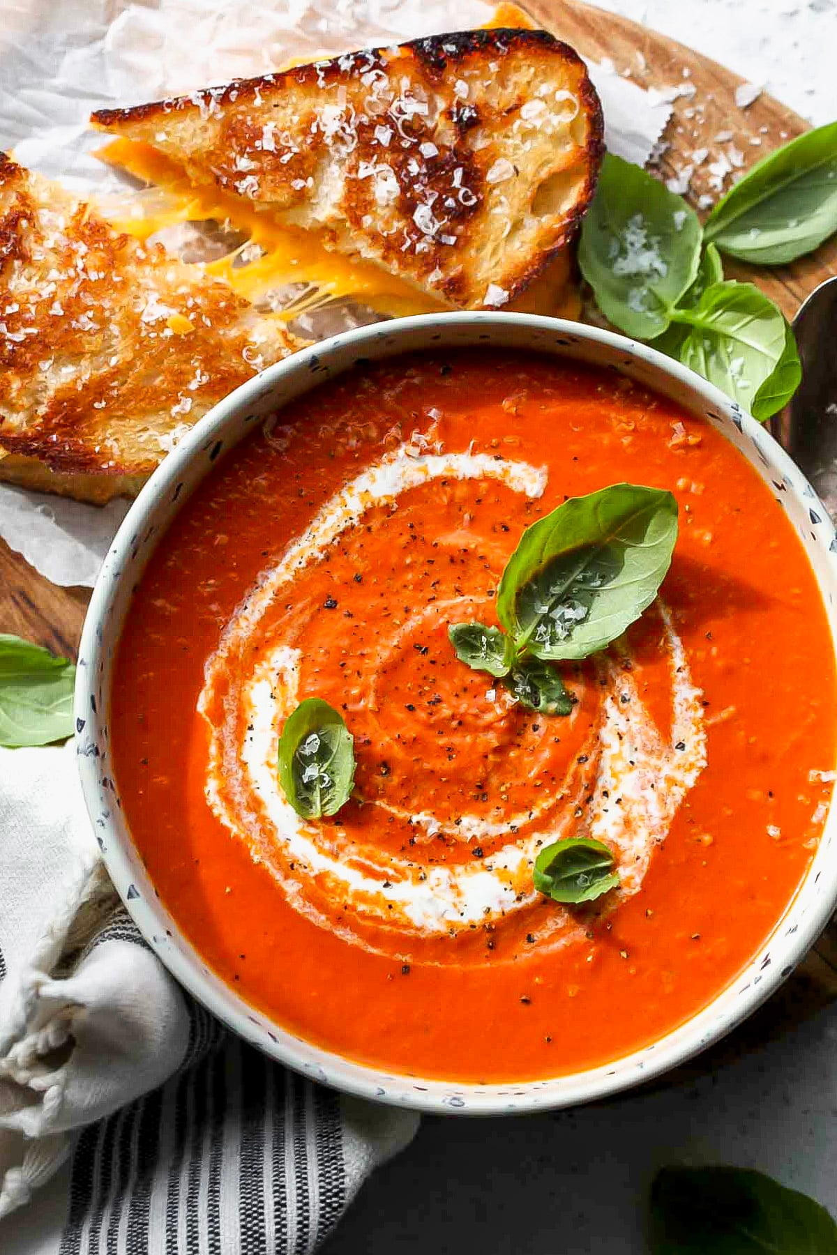 Tomato and red pepper soup styled in a white bowl with a grilled cheese resting on the side