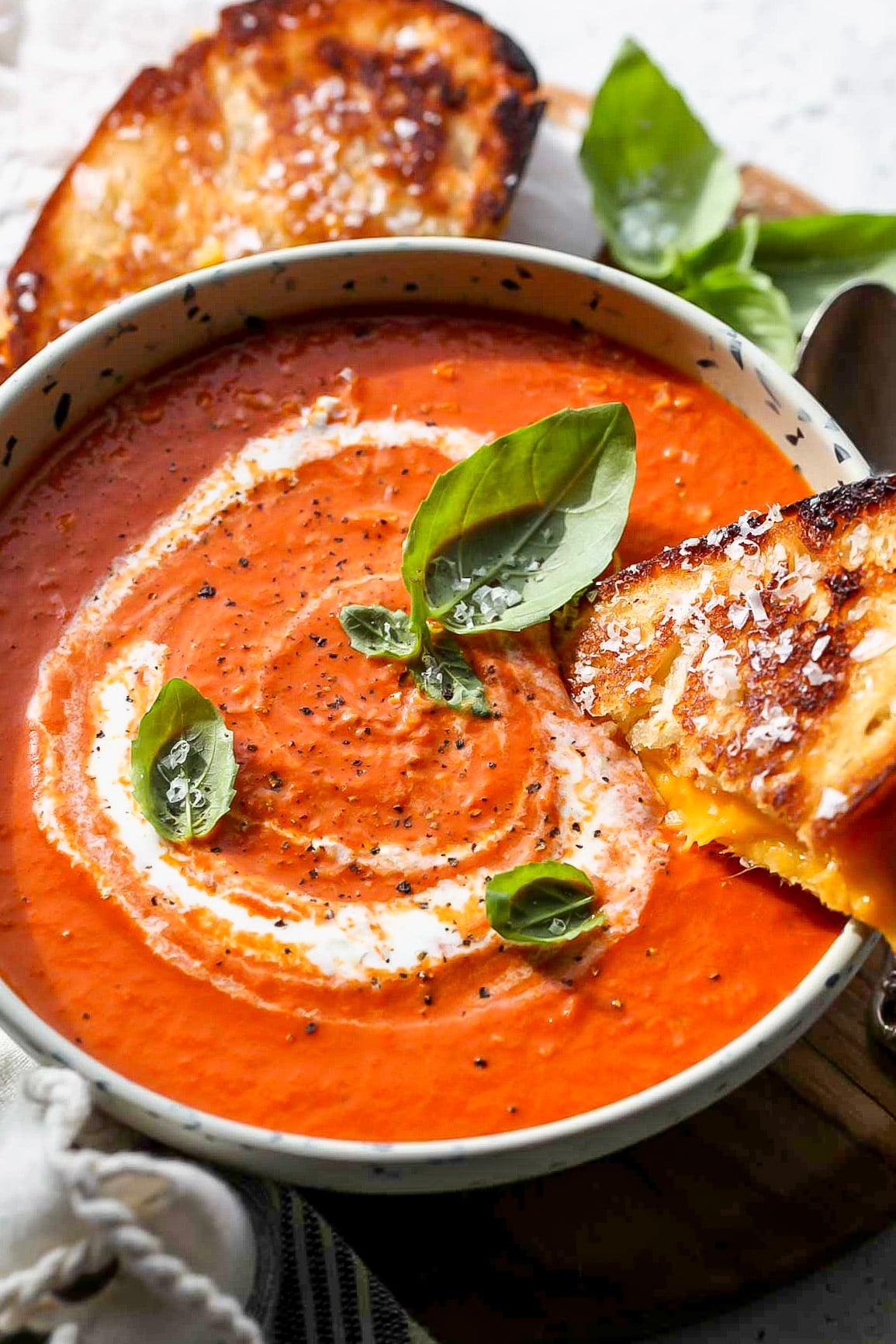 A bowl of tomato and roasted red pepper soup arranged on a cutting board topped with fresh basil leaves