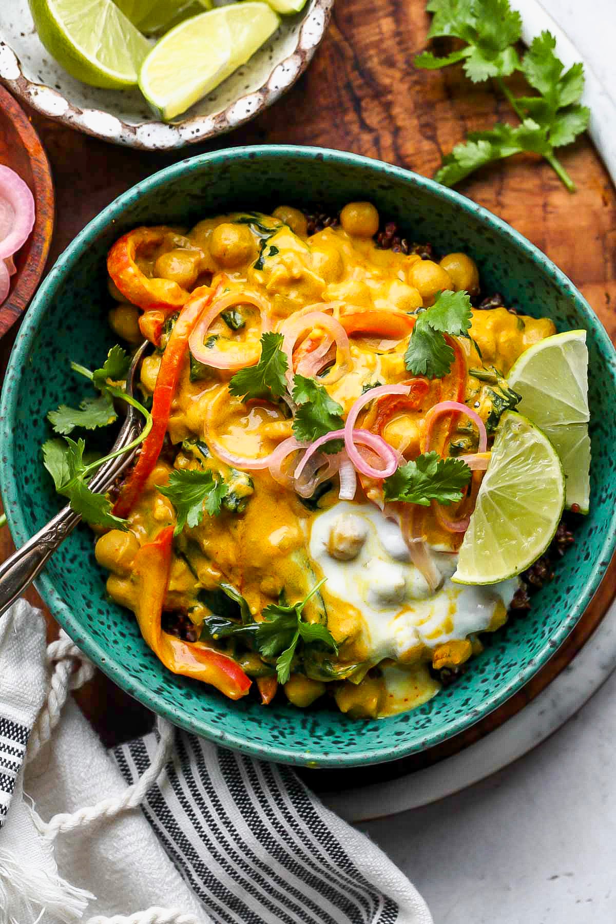 Vegan chickpea curry served over quinoa in a teal bowl topped with lime wedges and cilantro